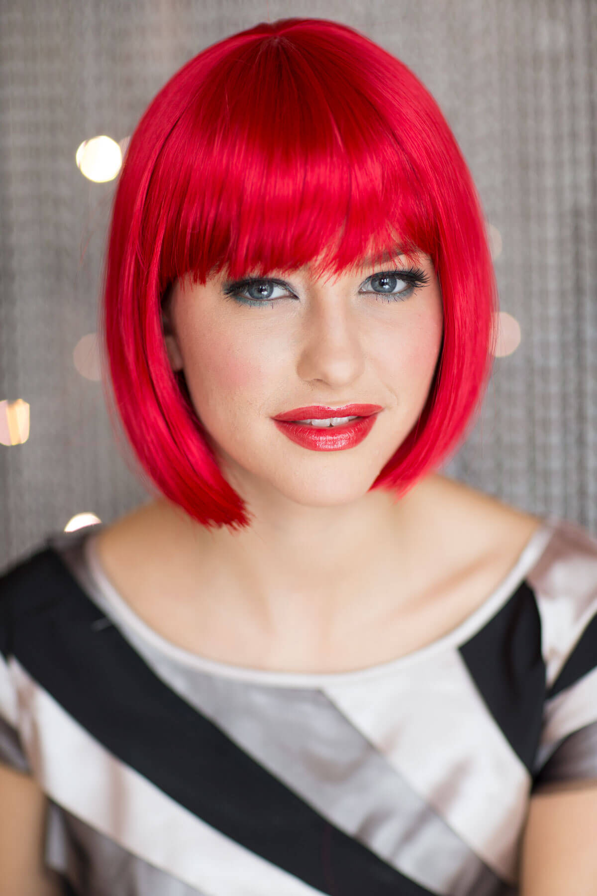 Woman with bright red hair and makeup wearing a black and white top. Vibrant, bright red bob wig: Maisy
