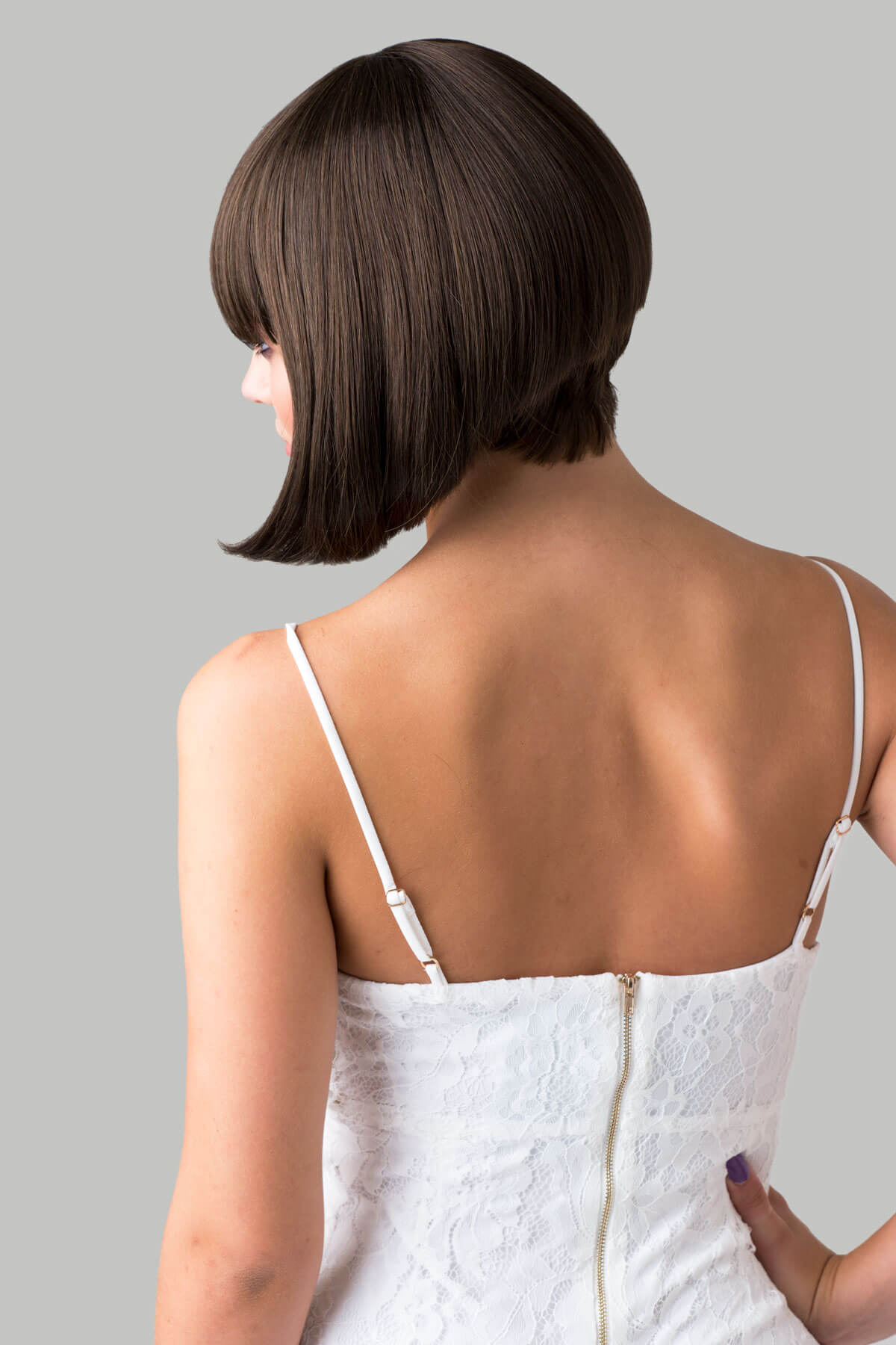 Woman wearing a white dress with thin straps against a gray background. Brown inverted bob wig: Colettechestnut brown 8