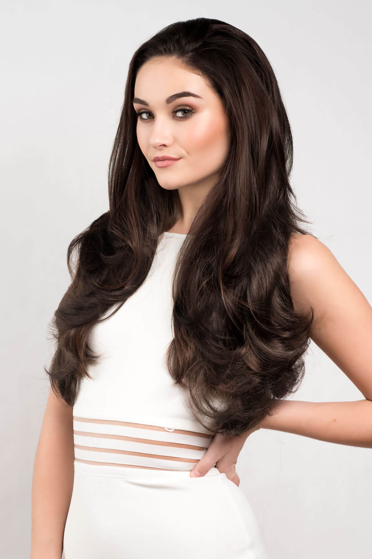 Woman with long, wavy brown hair wearing a white dress on a light gray background. Reddish brown half wig hairpiece with long, gentle waves: Heather dark brown 6 and reddish brown 33