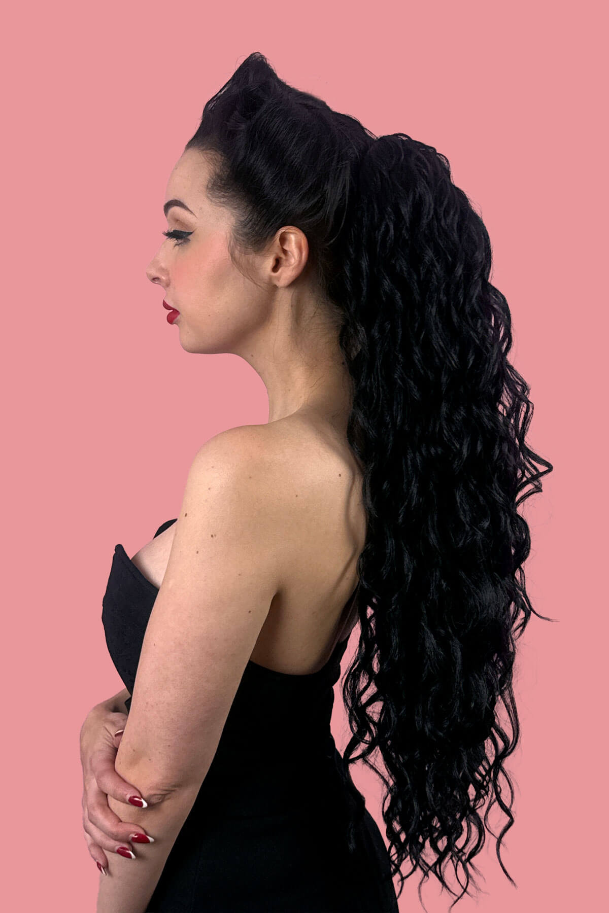 A woman in profile wearing a black strapless dress, showcasing a long, dark, curly wavy hair extension against a solid pink background. Long Curly Ponytail Hair Piece Extension, Black