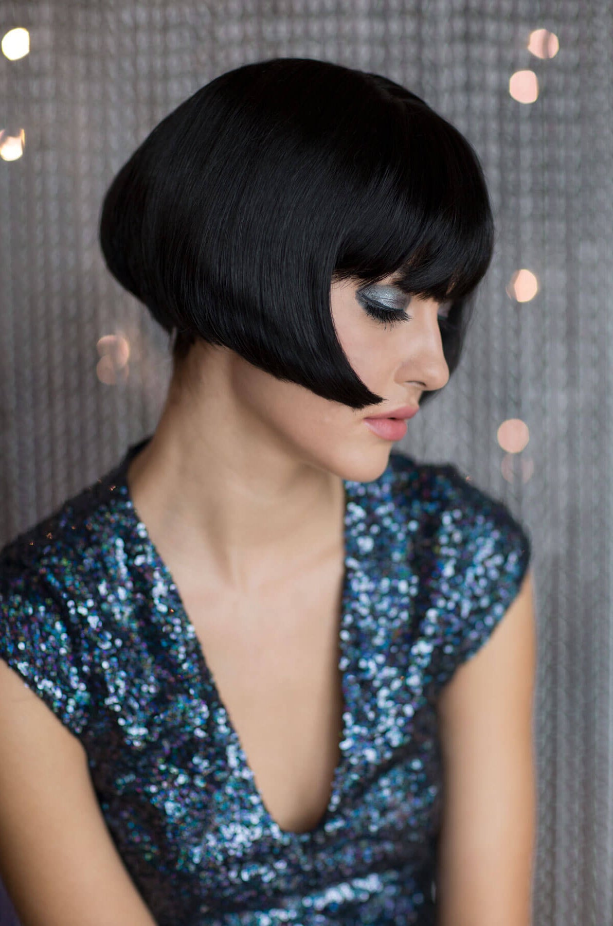 Woman with a stylish black bob haircut wearing a sequined dress against a textured wall. Louise Brooks style wig, short black bob: Brooks