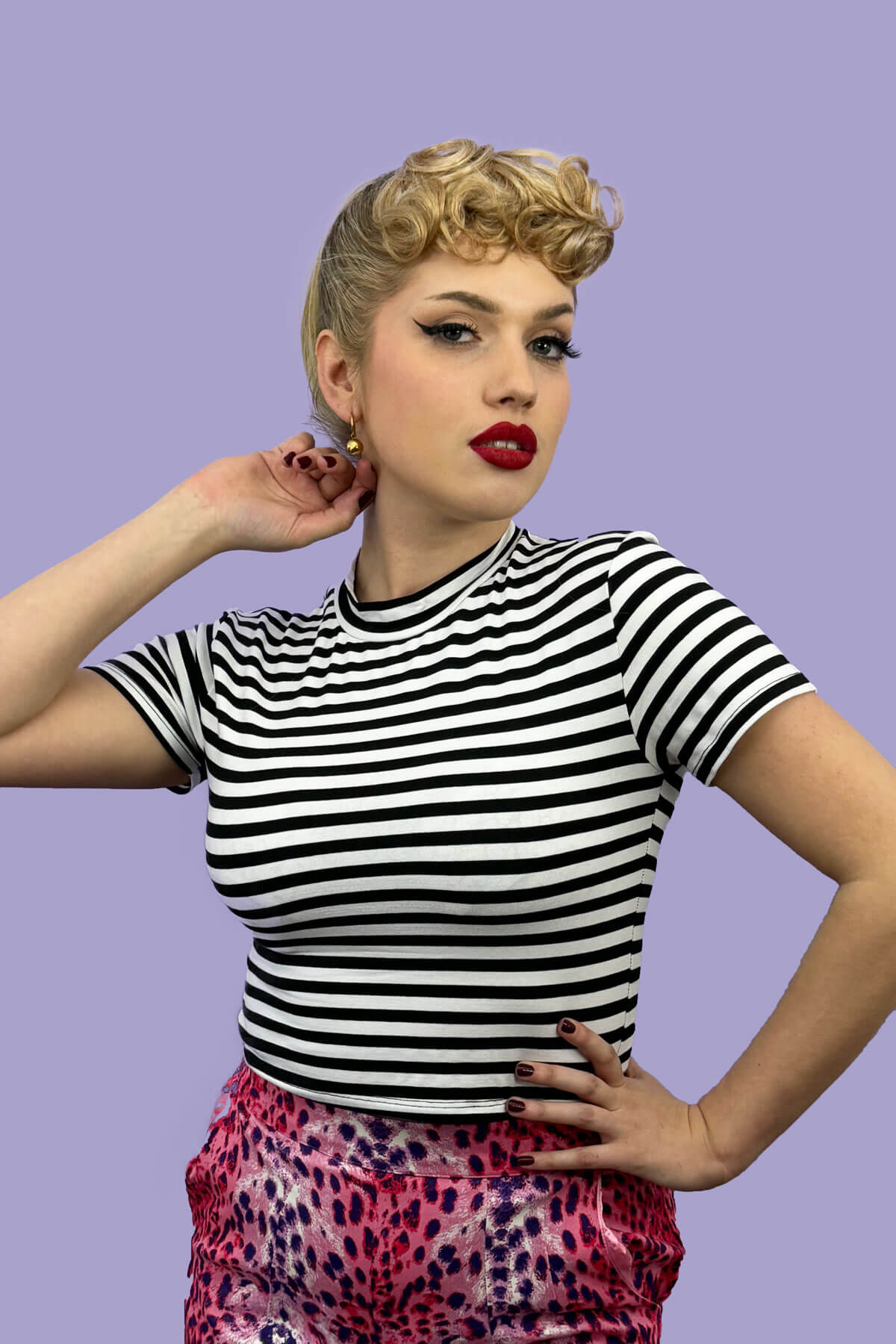 Woman wearing a black and white striped shirt with colorful pants against a purple background. Curly 1940s style clip-in fringe hairpiece/clip-in bangs: Bunny copper red 130