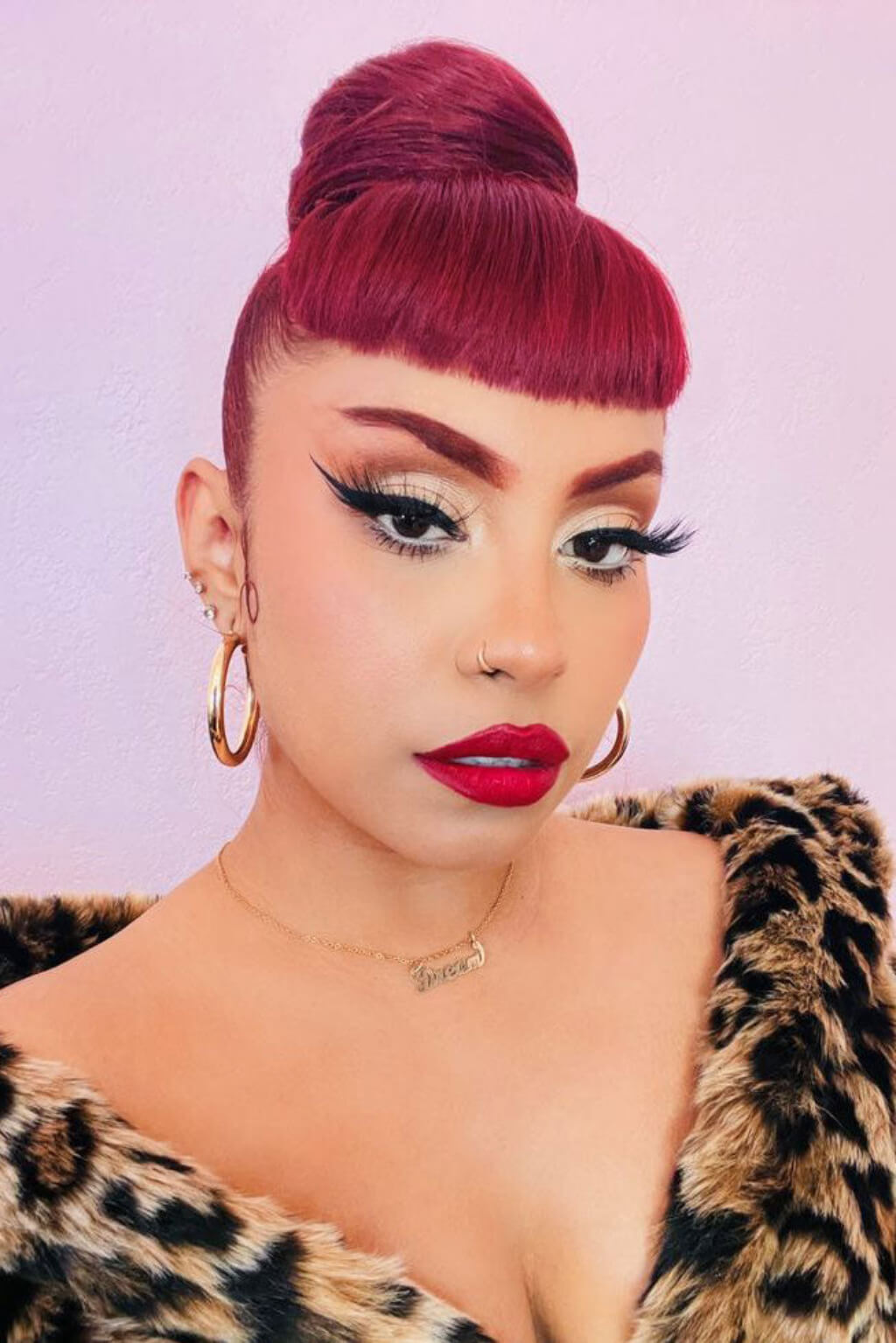 Woman with red hair styled in a bun, wearing a leopard print garment against a light purple background. Hairpiece bun; instant perfect bun hairpiece, cherry red: Hepburn