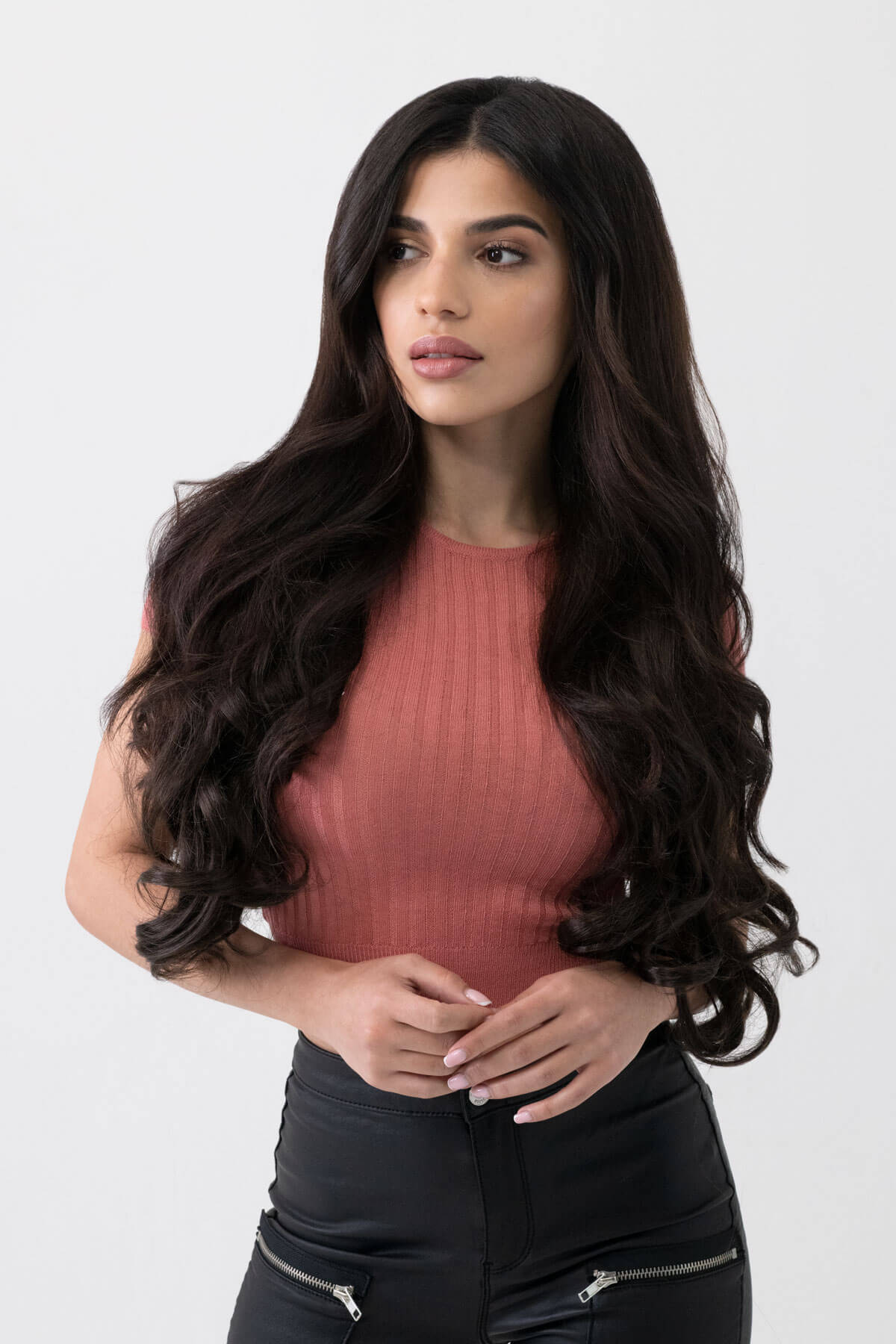 Woman with long, wavy hair wearing a pink top and black pants on a white background. synthetic hair extension set, 5 piece, 22 inches long, 300g