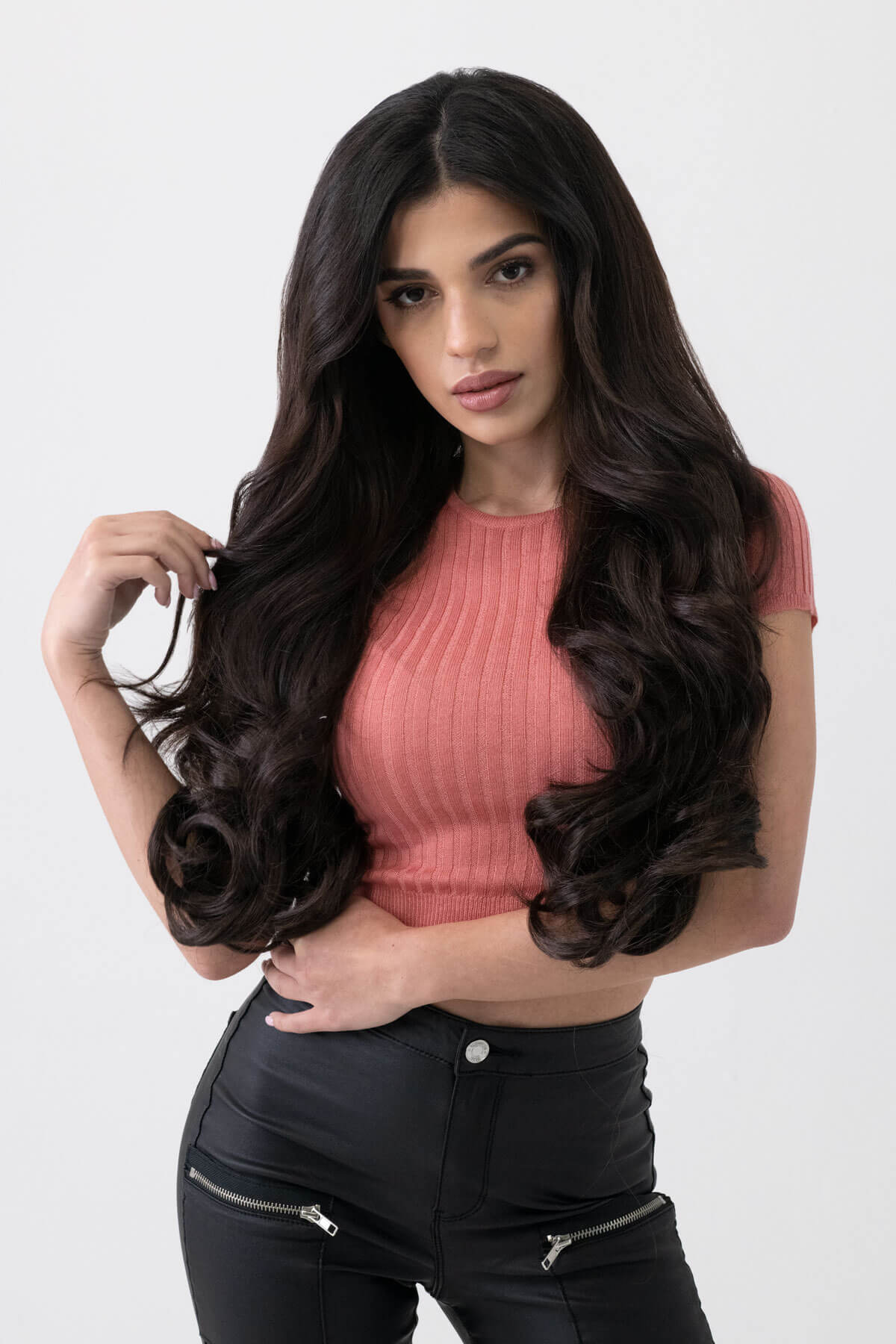 Woman with long, wavy hair wearing a pink top and black pants on a white background. 5 piece synthetic hair extension set, 22 inches long, 300g