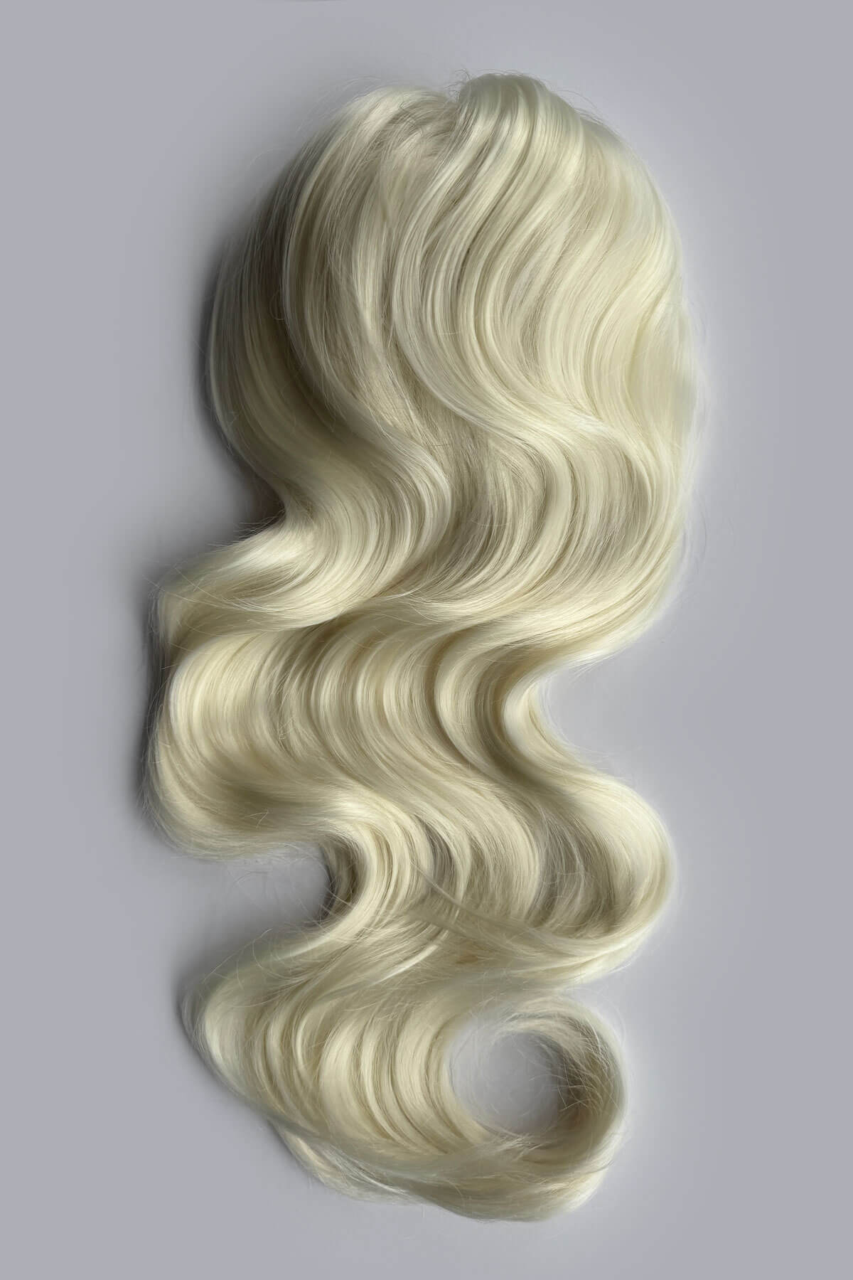 A long, wavy wig in a platinum blonde colour, displayed against a solid grey background. Double volume hairpiece extension: Naomi platinum blonde 1001
