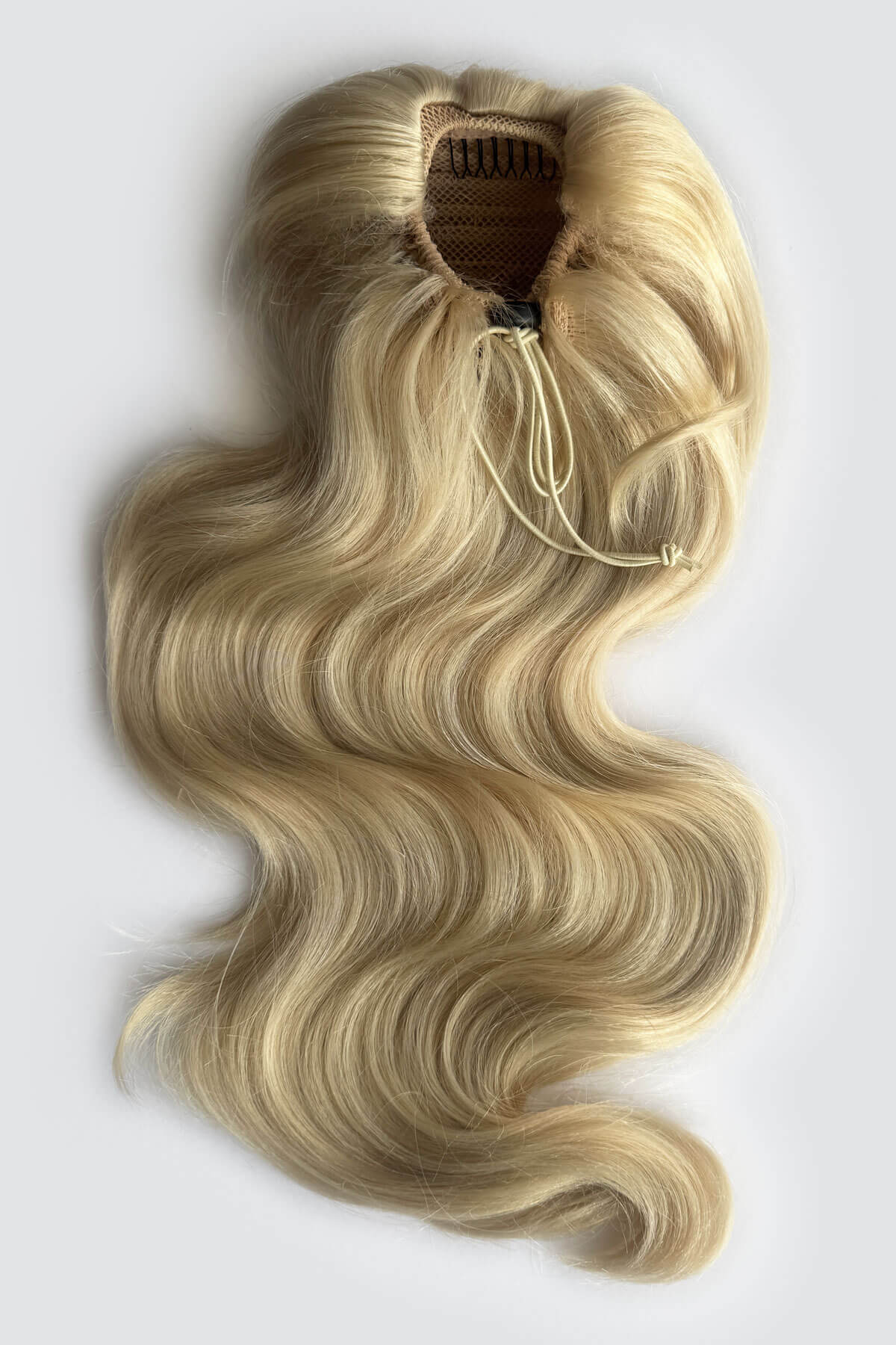 A long, wavy blonde hair extension piece with a draw string attachment, photographed against a plain light grey background. Double volume hairpiece extension with gentle waves: Naomi blonde 613