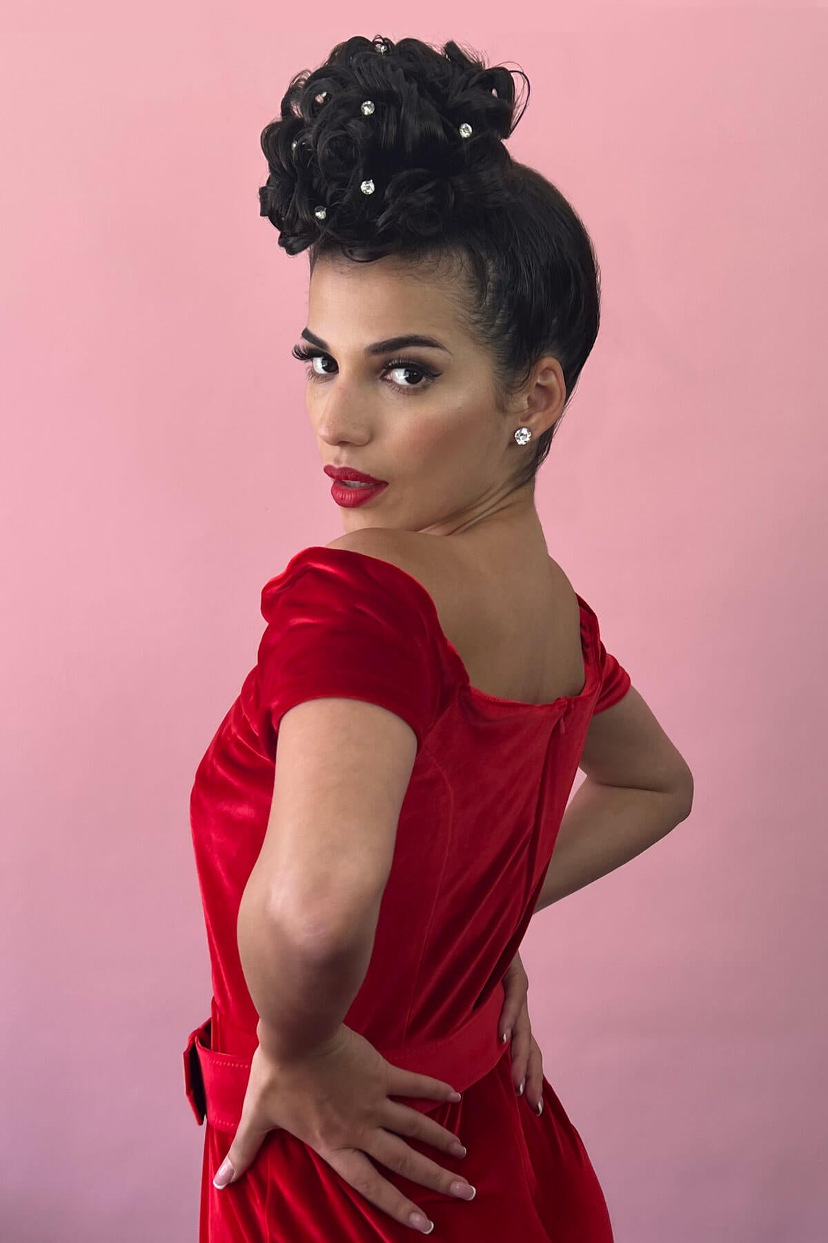 Woman in a red dress with a pink background. Hair poodle clip-in hairpiece bun vintage style 1950s: Lucille jet black 1