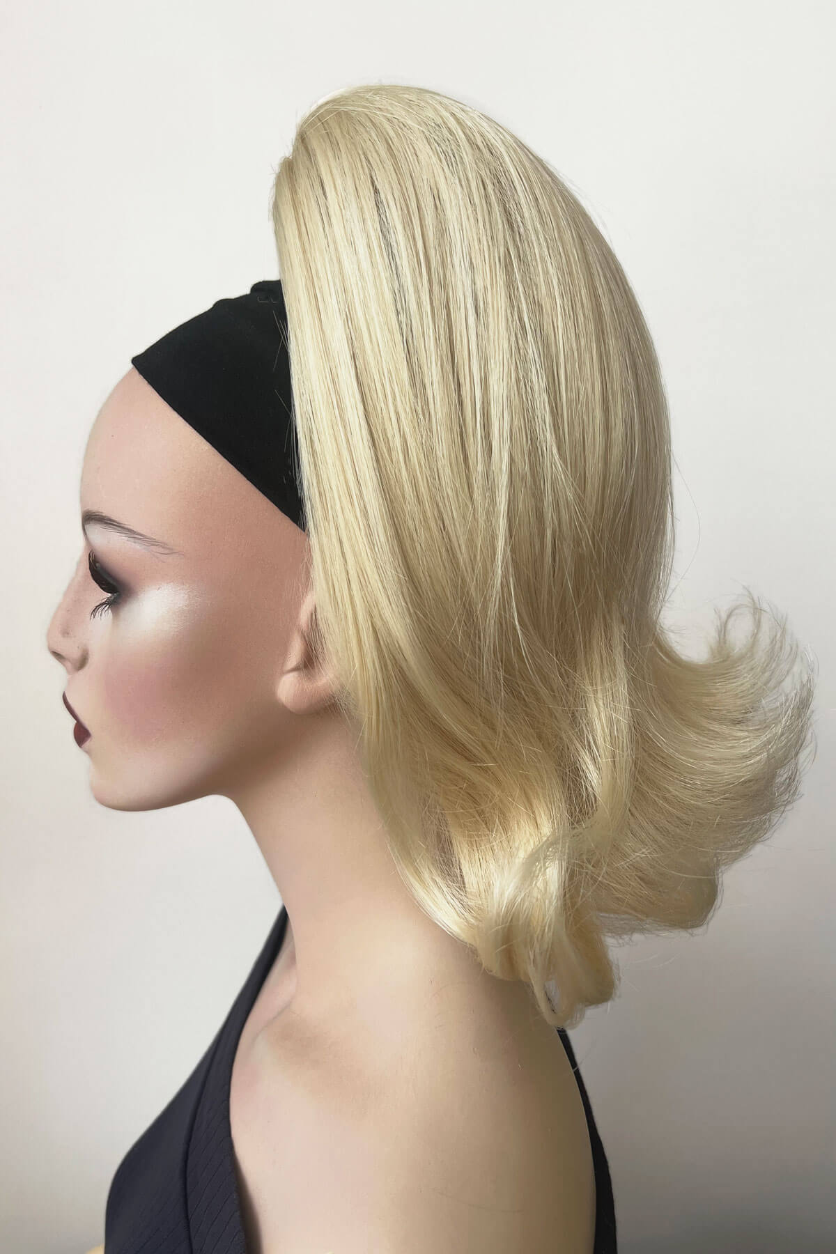Mannequin head with blonde wig on a plain background. Ponytail hairpiece, shoulder length with flick/flip, retro 1960s style: Ariana creamy blonde 613