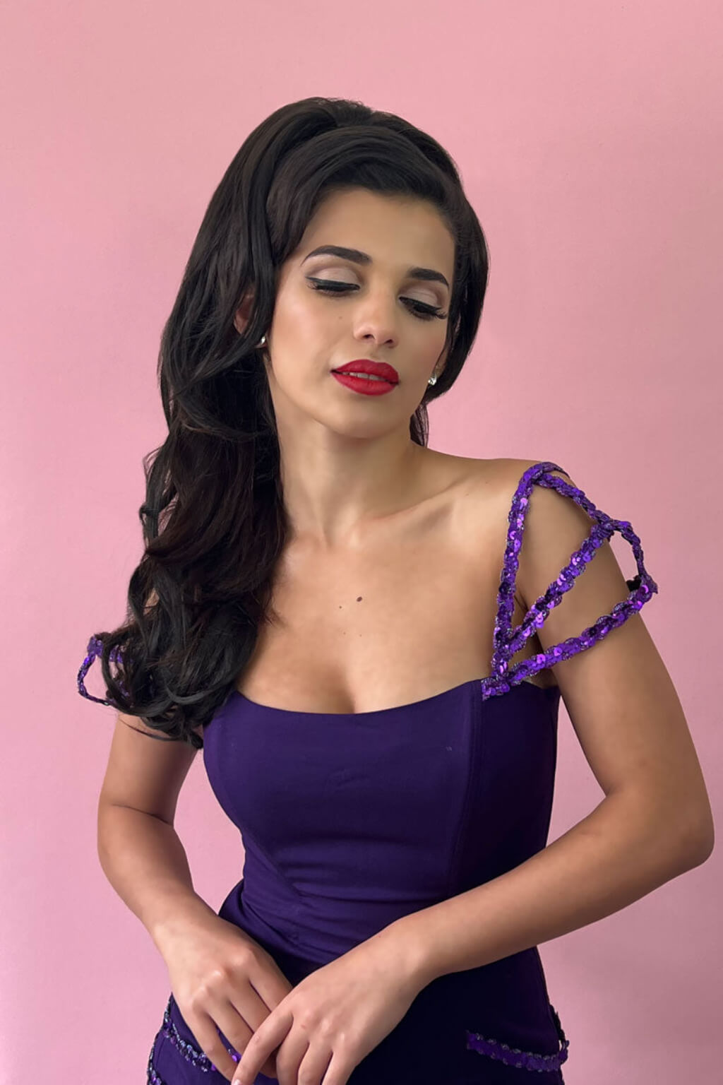 A woman with long dark wavy hair models a deep purple off-the-shoulder dress with textured purple shoulder straps against a solid pink background. Double volume hairpiece extension: Naomi dark brown 4