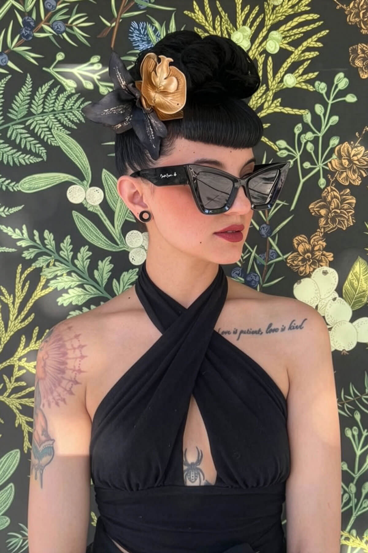 Woman wearing a black dress and sunglasses with a floral headpiece against a decorative background. Hair poodle clip-in hairpiece bun vintage style 1950s: Lucille black 1B