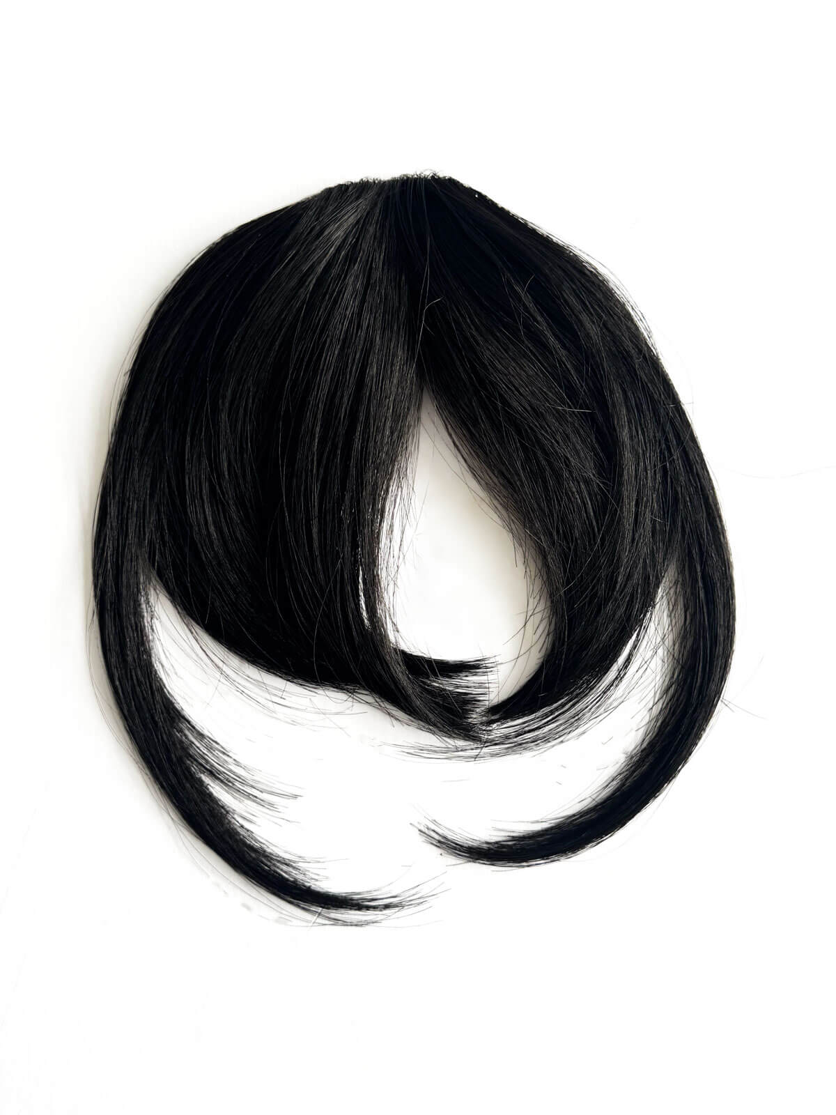 Black hair extension on a white background. Clip in fringe hairpiece/clip-in bangs, gently feathered with face framing whisps: Delia black 1B