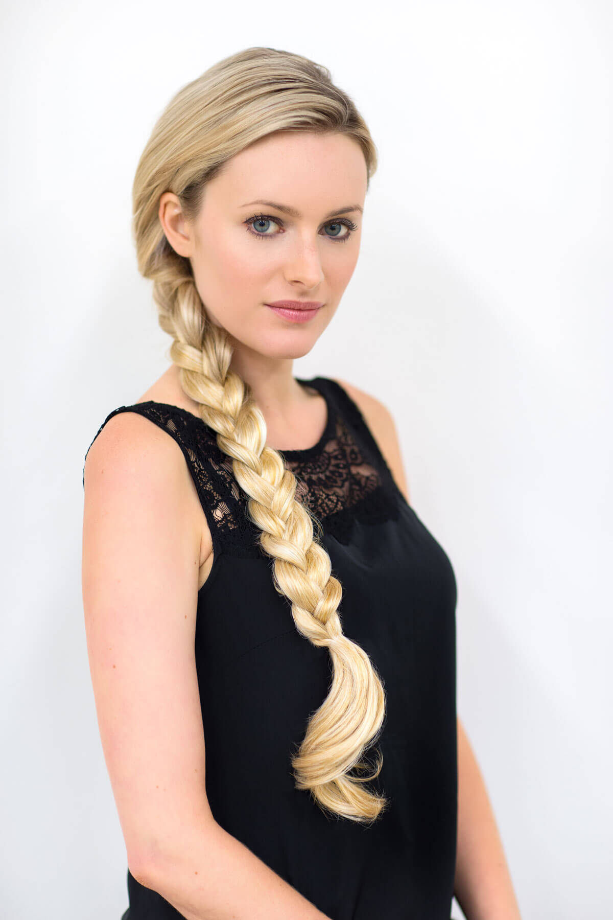 Woman with long blonde braided hair wearing a black sleeveless top on a white background. Extension hairpiece, long, versatile, Flexihair: Cristina honey blonde 24BH613