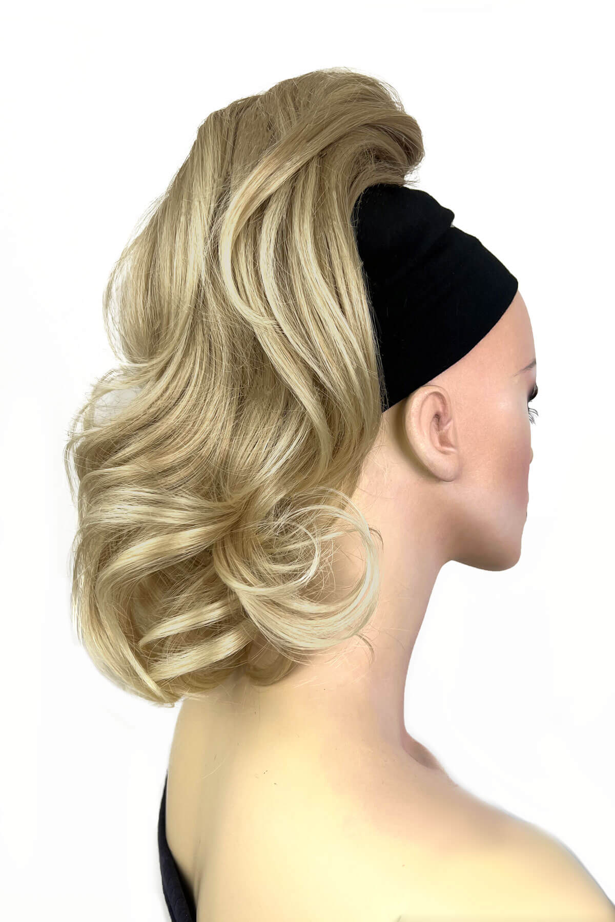 A woman wearing a curly ponytail extension hairpiece with loose, layered curls. She is seen from the shoulders up. Curly ponytail extension clip-on hairpiece: Tulisa blonde 613T24