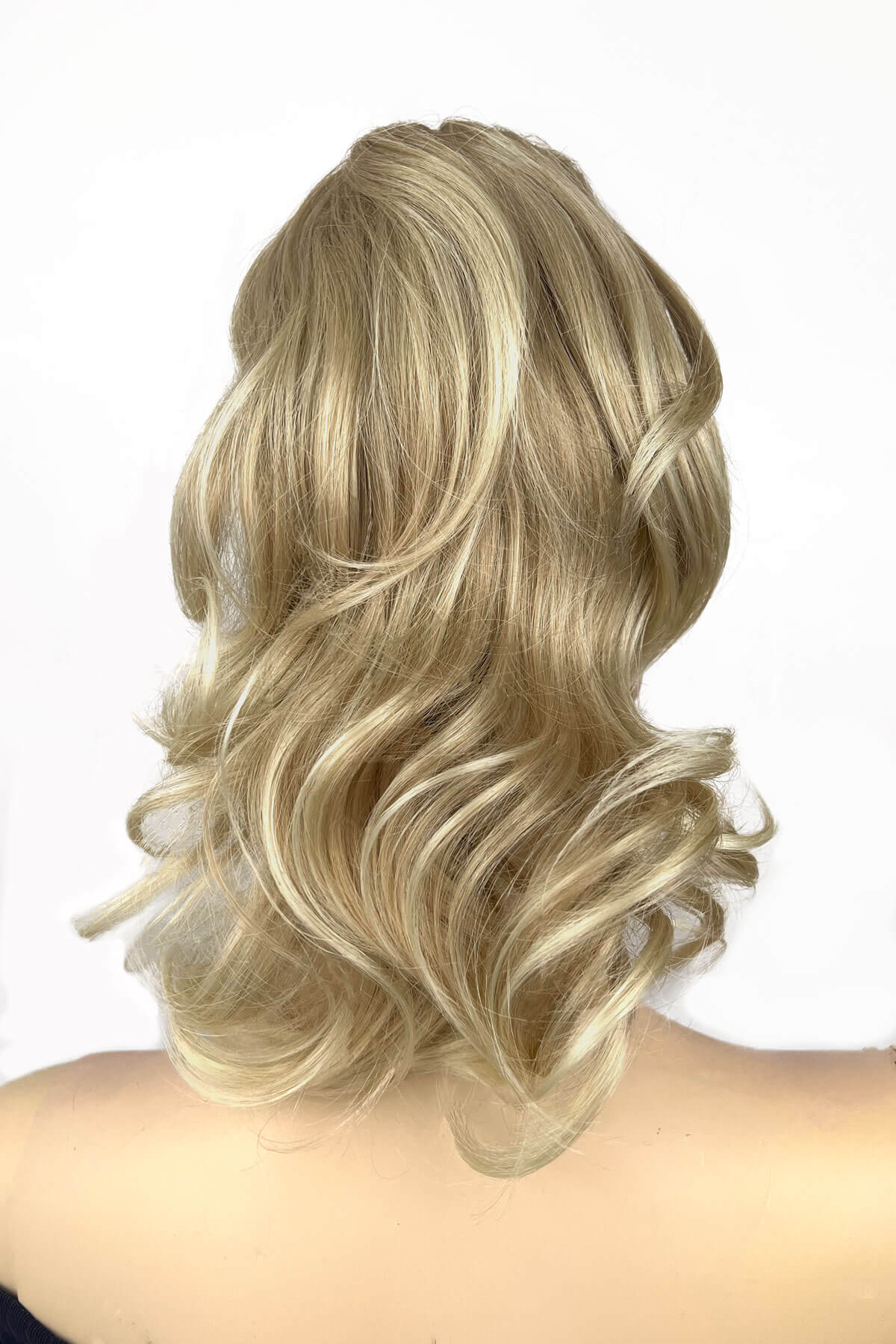 A woman wearing a curly ponytail extension hairpiece with loose, layered curls. She is seen from the shoulders up. Curly ponytail extension clip-on hairpiece: Tulisa blonde 613T24