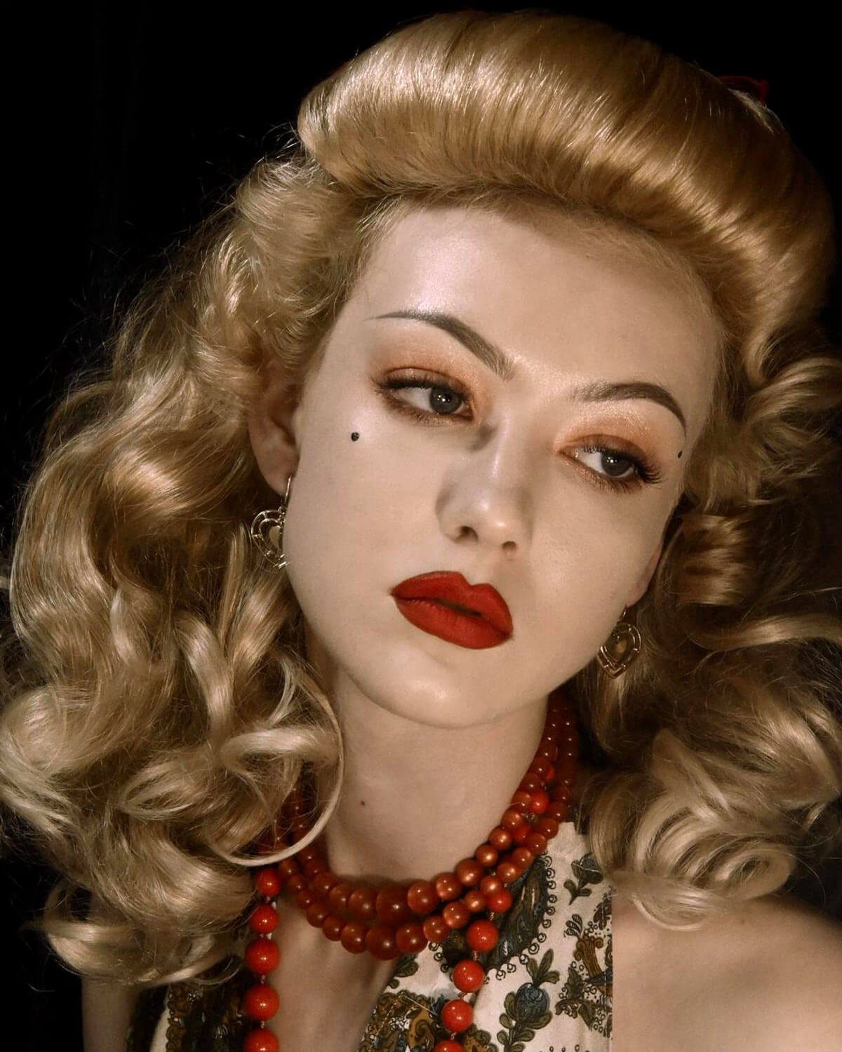 Woman with vintage-style hair and red lipstick wearing a necklace against a dark background. Bumper bangs pack - vintage 40s 50s fringe roll: Lena blonde 24H613