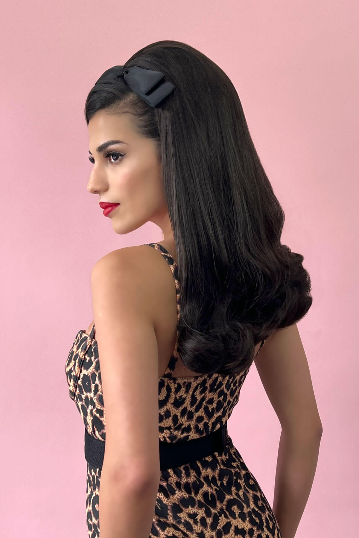 Woman with long, wavy hair wearing a black headband against a pink background. 1960s Retro high crown, half wig hairpiece, long with hair flip: Priscilla chocolate brown 6