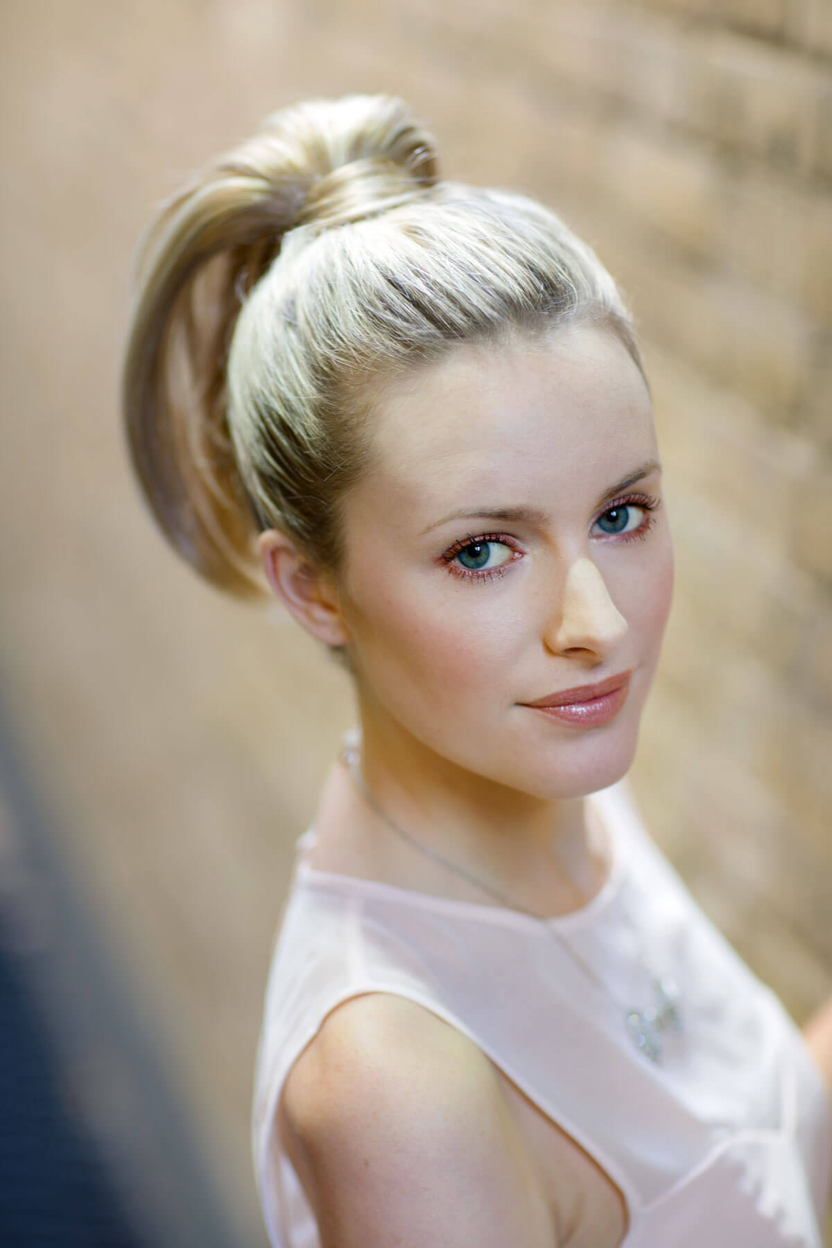 Woman with blonde hair styled in a bun wearing a light pink top. Sleek ponytail extension hairpiece, Flexihair: Jasmin