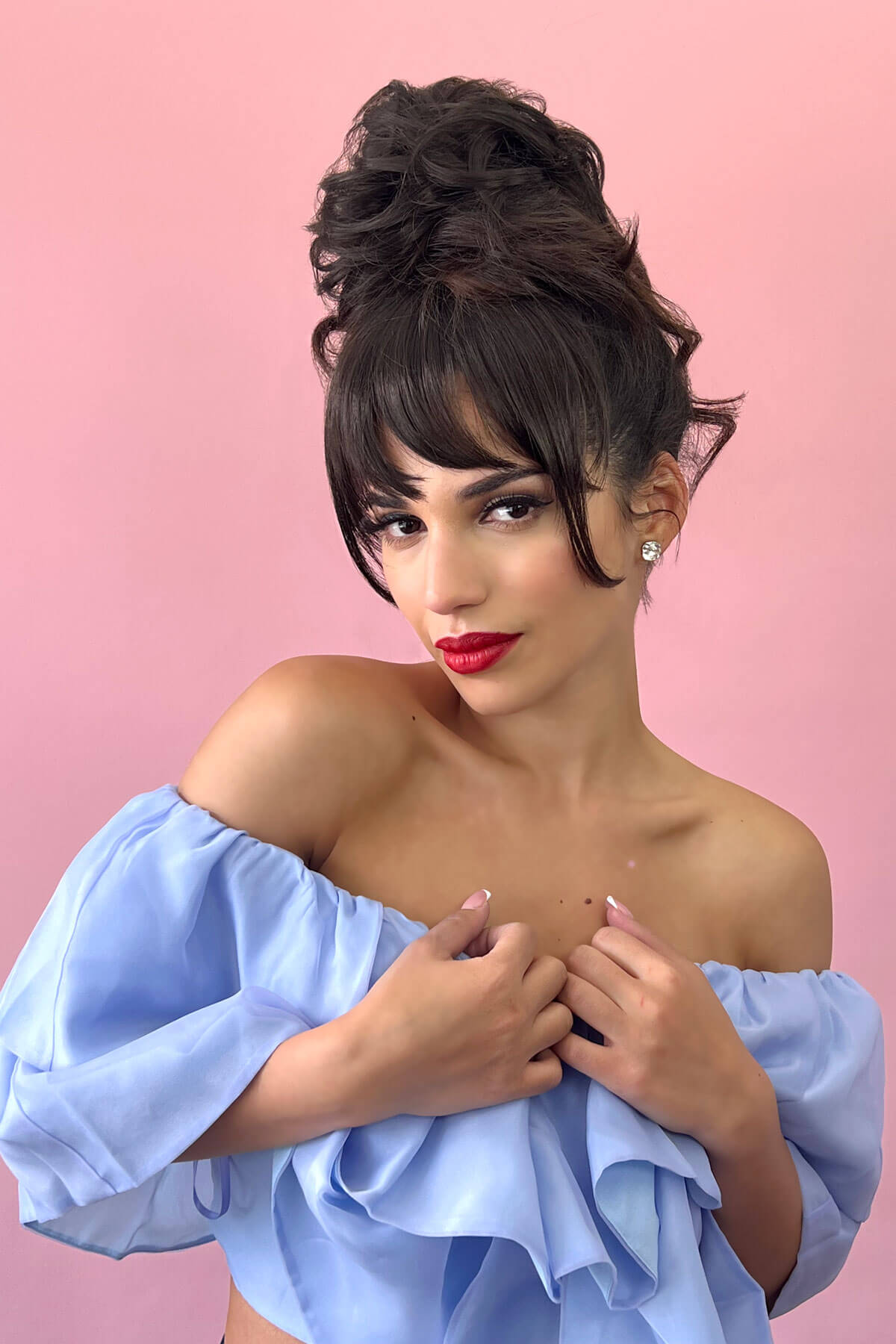 Woman with styled hair and red lipstick wearing a light blue off-shoulder top against a pink background. Scrunchie bun hairpiece, easy updo messy bun: Betsy copper red 130