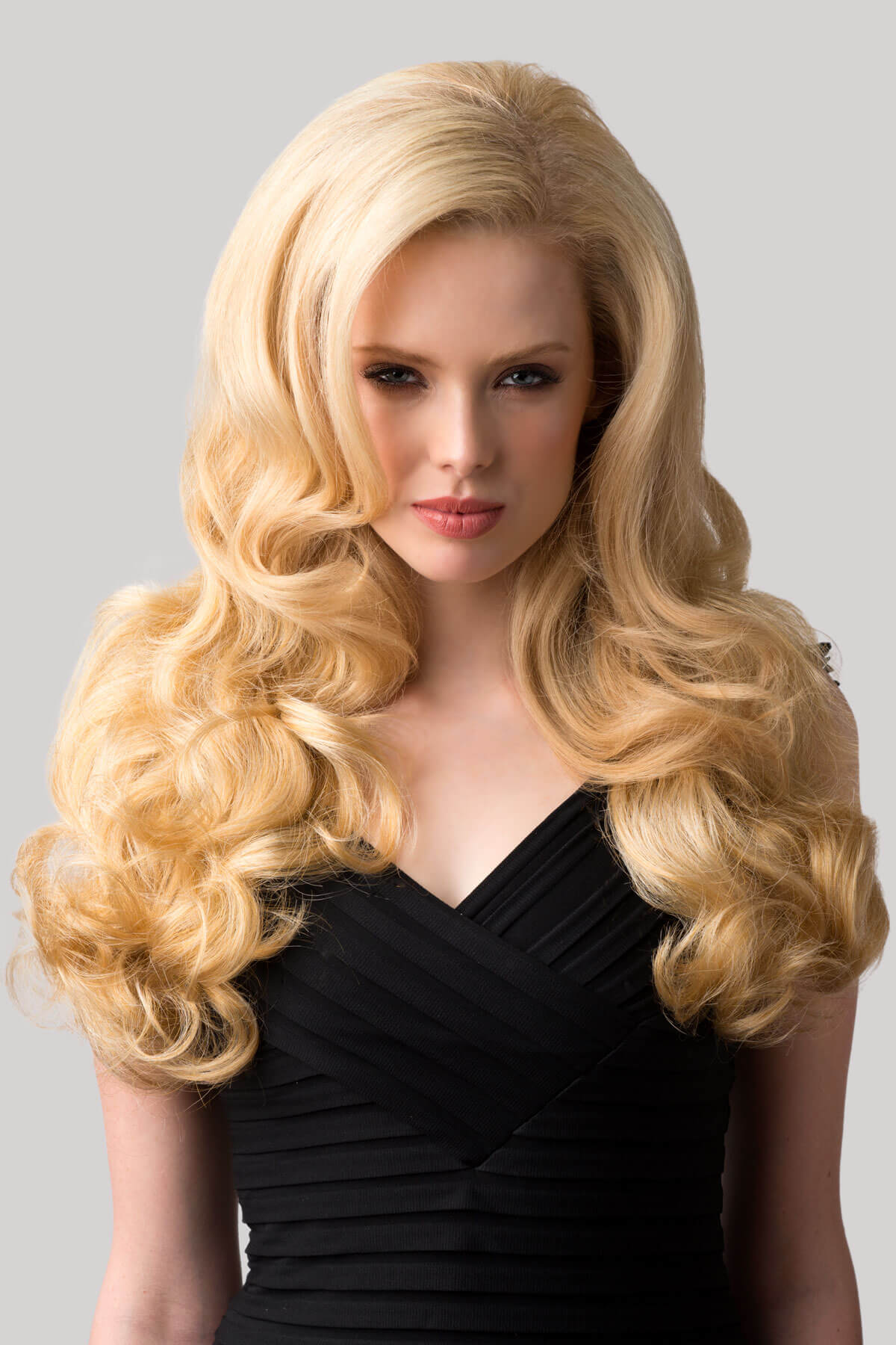 Woman with long blonde hair styled in curls wearing a black dress on a gray background. Curly blonde half wig hairpiece extension (3/4 wig), long: Meana honey blonde 24BH613