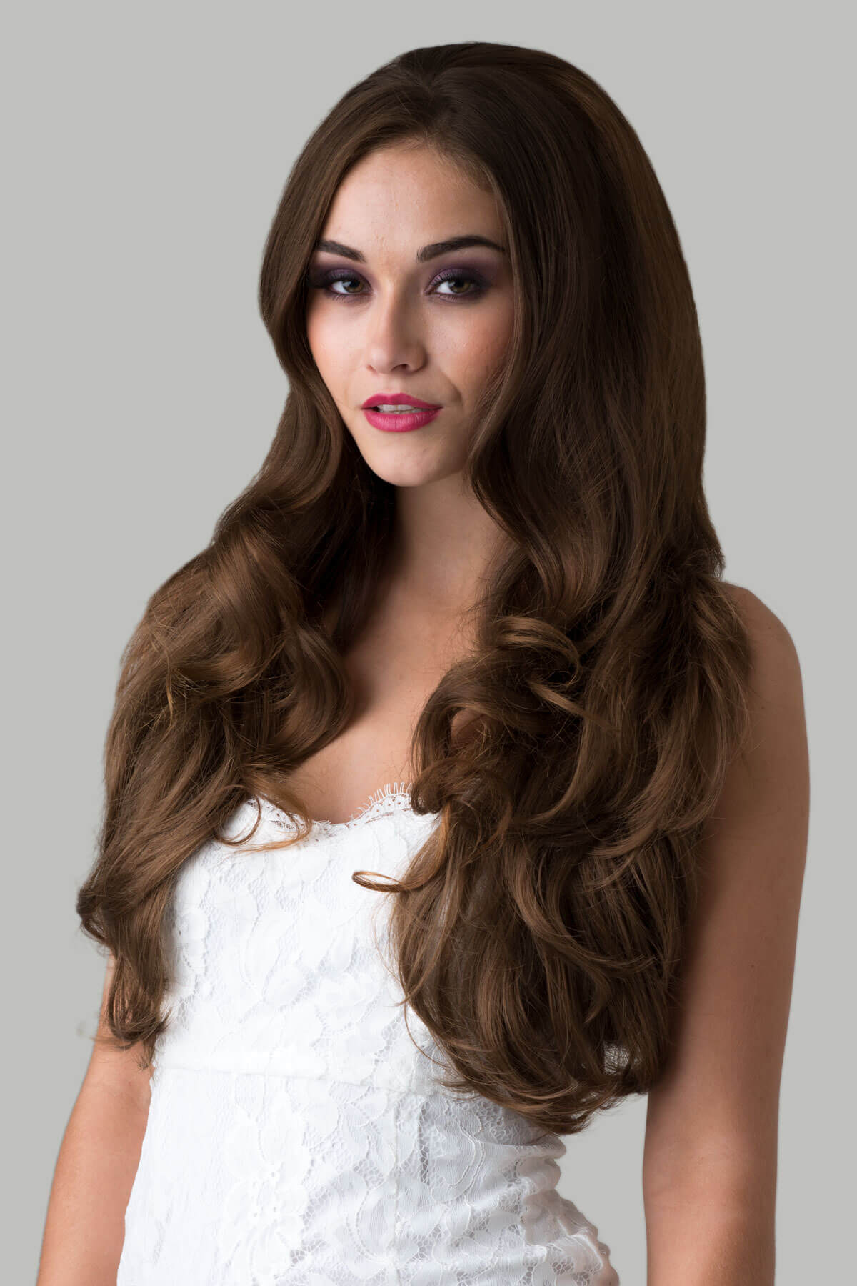 Woman with long, wavy brown hair wearing a white dress on a gray background. Brown half wig hairpiece (3/4 wig), layered, wavy: Simone light brown 12