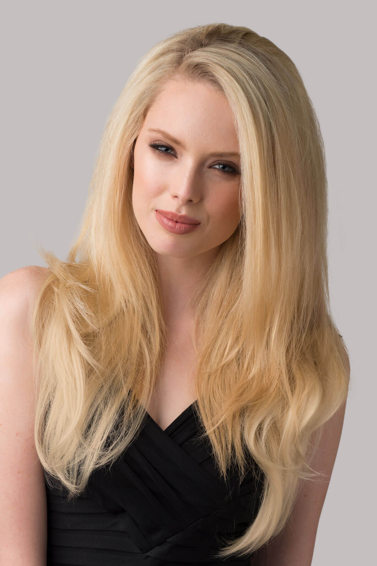 Woman with long blonde hair wearing a black top against a gray background. Straight blonde half wig hairpiece (3/4 wig), layered: Autumn blonde 24BT613
