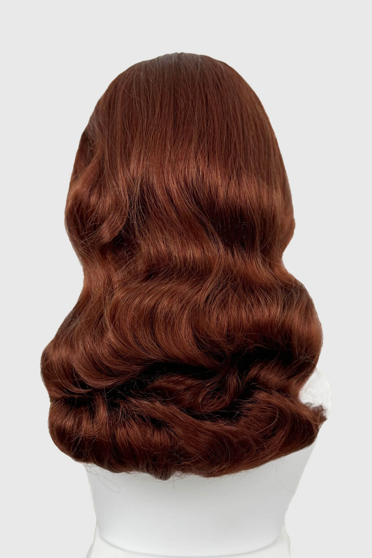 Copper red wig on a white mannequin head against a white background. 1950s style half wig hairpiece with beautiful waves: Morgana copper red 130