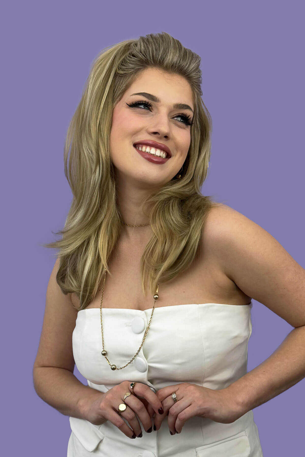 Woman in a white strapless top against a purple background. Half wig hairpiece, long and wavy, Flexihair (Heat styleable) and volume ring for high crown: Sharon blonde 24H613
