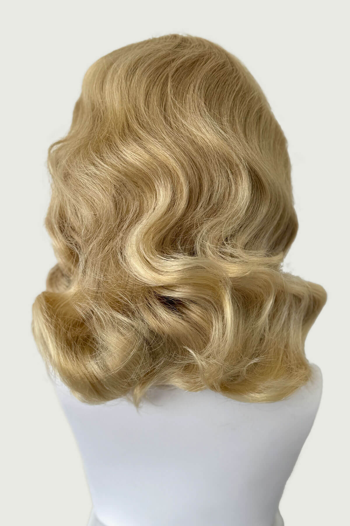 Blonde wig on a mannequin head against a white background, viewed from the back. 1950s style shoulder length half wig hairpiece with beautiful vintage waves: Onyx blonde 613T24