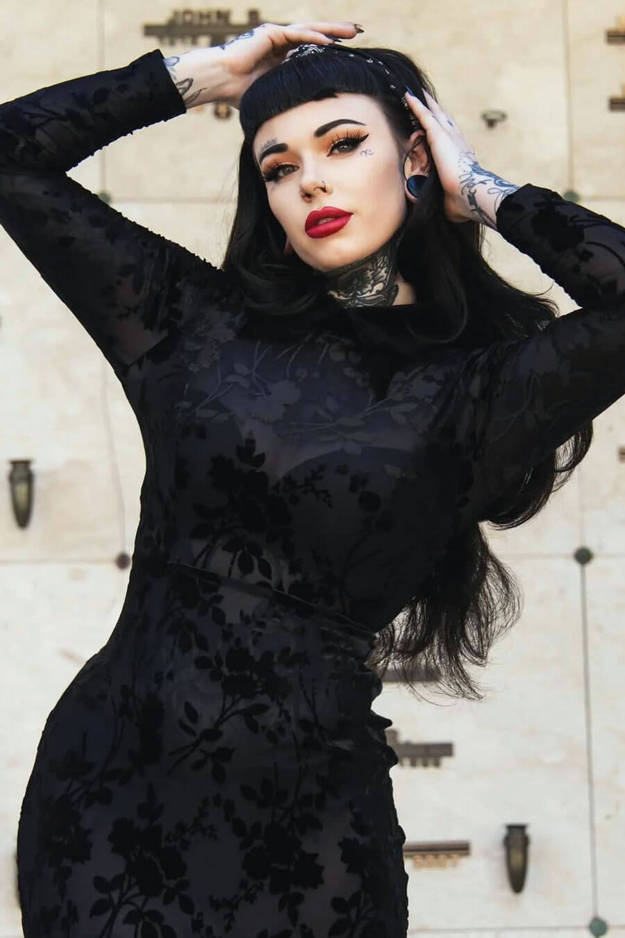 Woman in a black lace dress posing against a textured wall. Black half wig hairpiece (3/4 wig), long layers: Aislynn