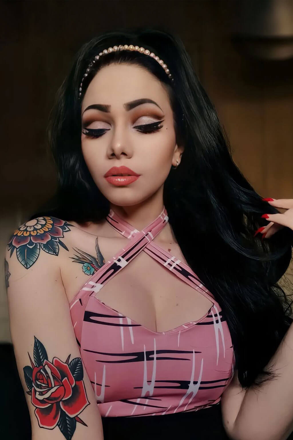 Woman with tattoos and a pink top posing indoors. High crown long, wavy half wig and volume ring: Bardot black 1B