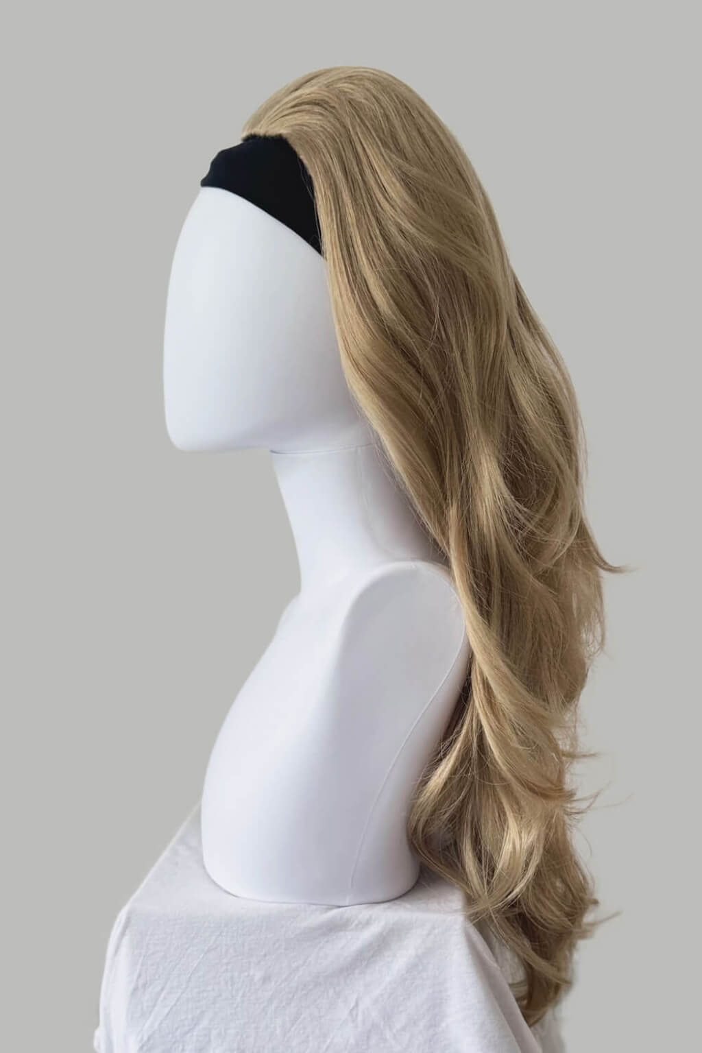 A long, wavy blonde wig displayed on a white mannequin head against a grey background. High crown long, wavy half wig and volume ring: Bardot blonde 24H613