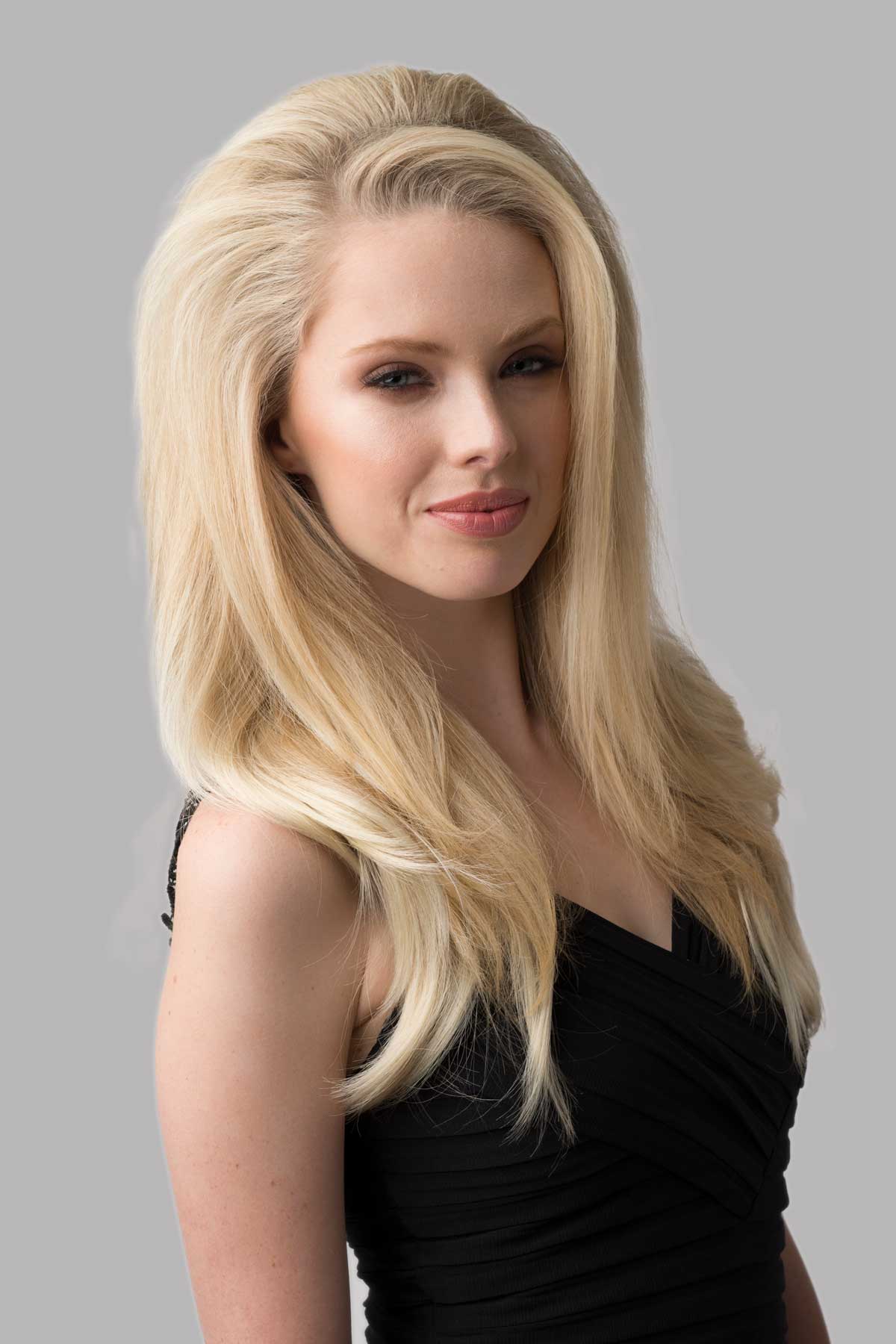 Woman with long blonde hair wearing a black top against a gray background. Straight half wig with high crown; height boosting technology: Claudia blonde 613T24