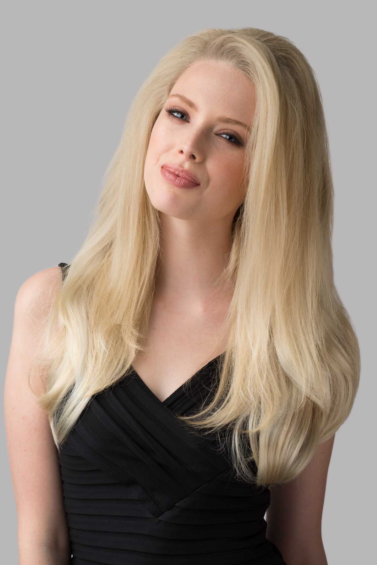 Woman with long blonde hair wearing a black dress against a gray background. Straight half wig with high crown; height boosting technology: Claudia blonde 613T24