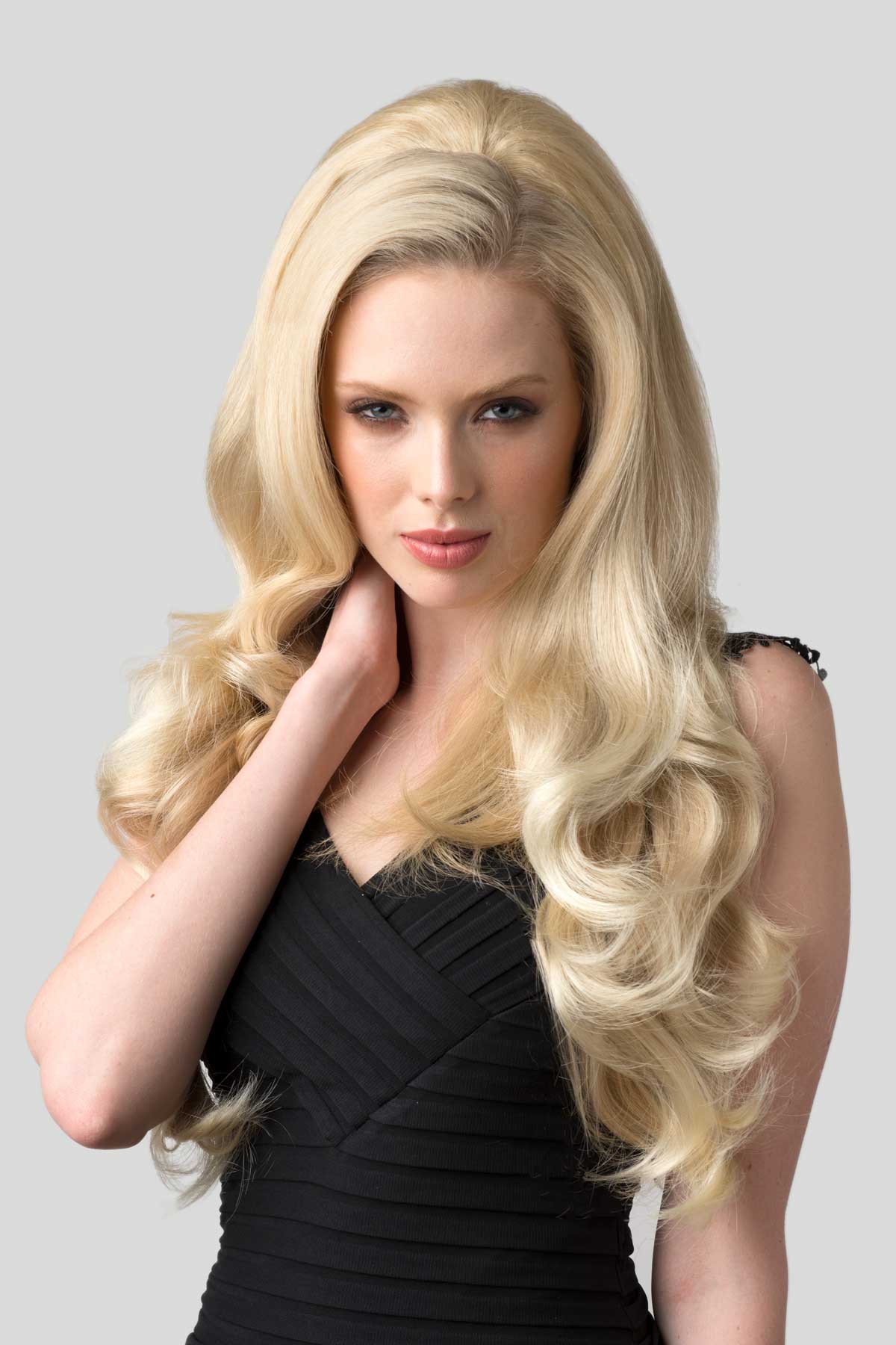 Woman with long blonde hair wearing a black dress against a gray background. Half wig with volume booster/height booster: Corrine blonde 613T24