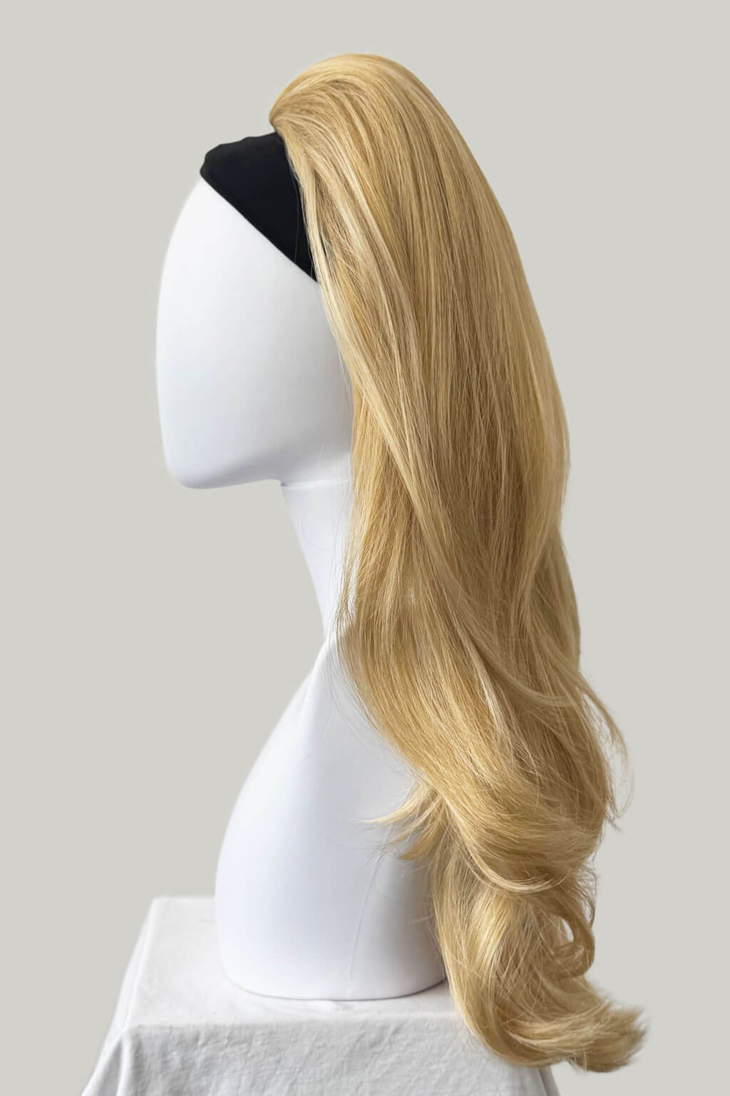 Blonde wig on a mannequin head against a plain background. 1960s style hair, high crown long straight and layered half wig: Juliette golden blonde 24BH613