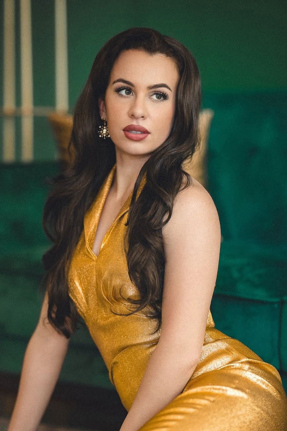Woman in a gold dress sitting on a green couch. Brown half wig hairpiece, full, long with gentle waves: Taya chestnut brown 8