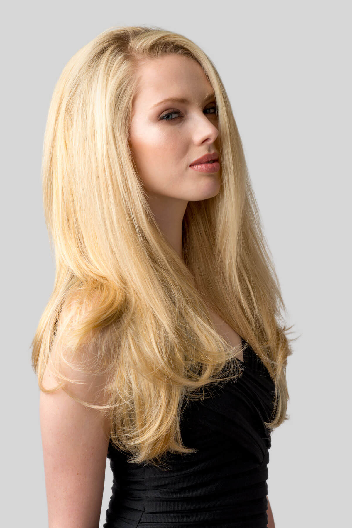 Woman with long blonde hair against a gray background. Straight blonde half wig hairpiece (3/4 wig), layered: Autumn honey blonde 24BH613