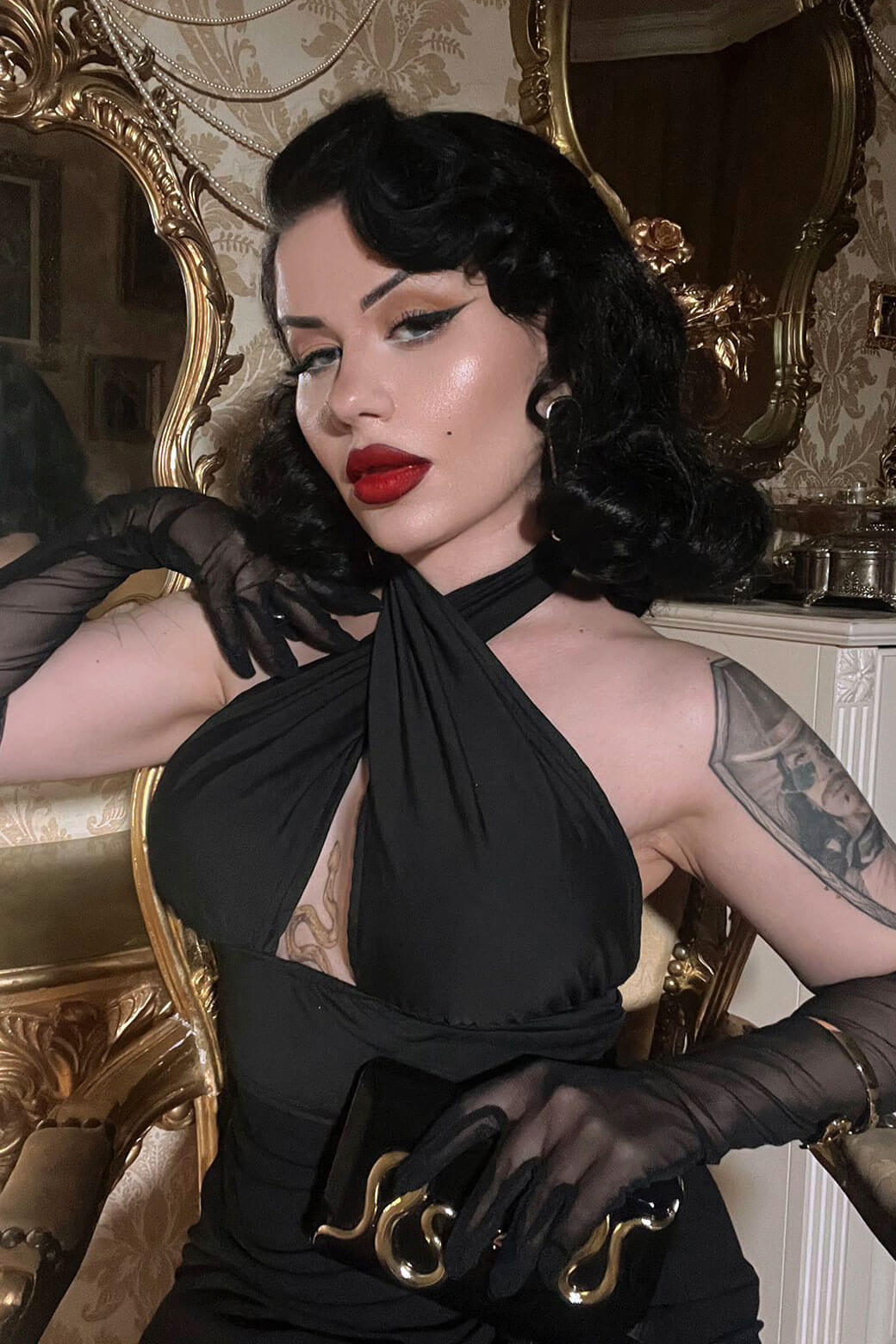 Woman in a black dress with red lipstick and black gloves in an ornate room. 1940s style half wig hairpiece with beautiful marcel waves: Virginia jet black 1