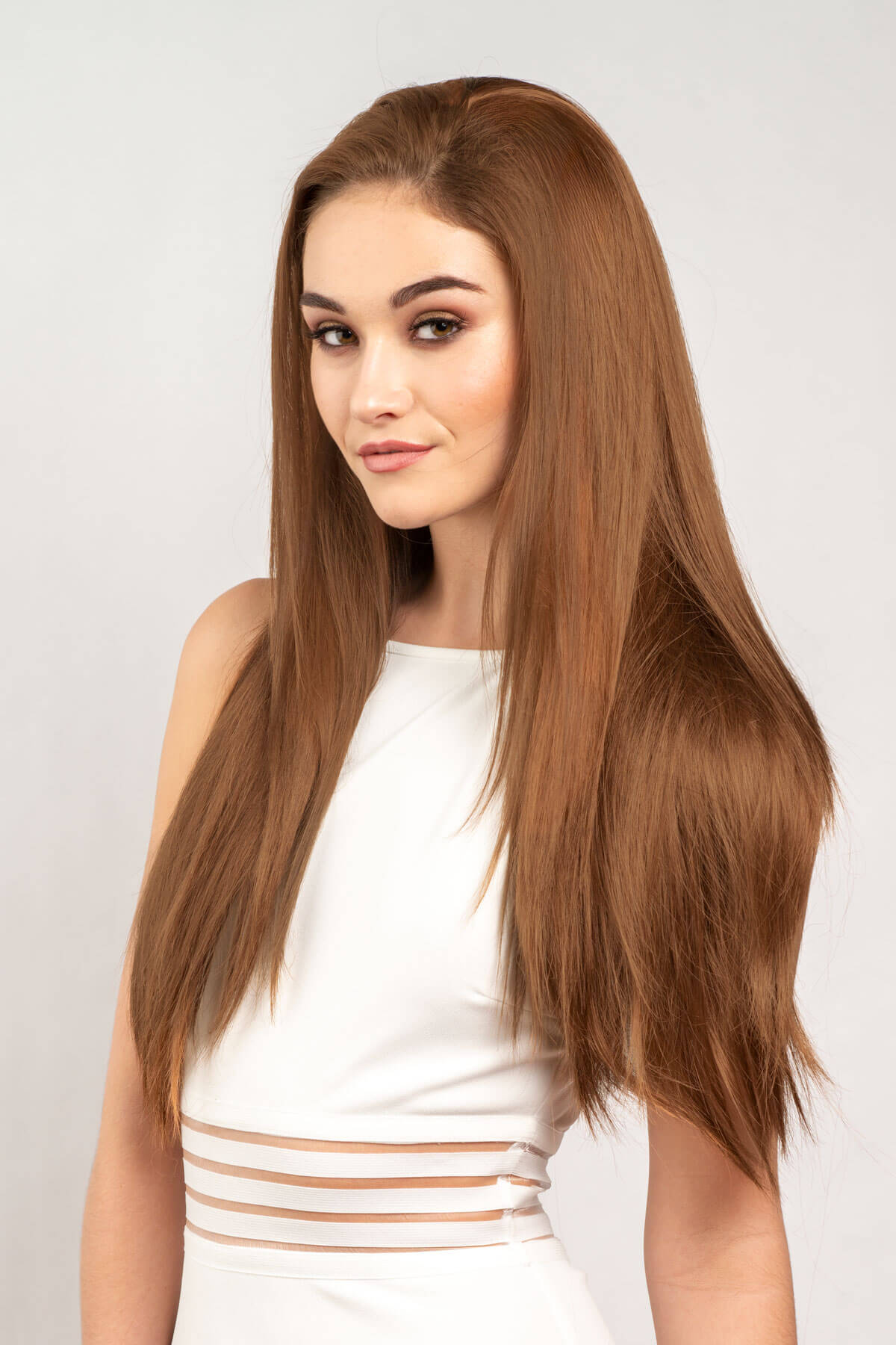 Woman with long brown hair wearing a white top against a light gray background. Straight brown half wig hairpiece extension, long: Faye auburn brown 30