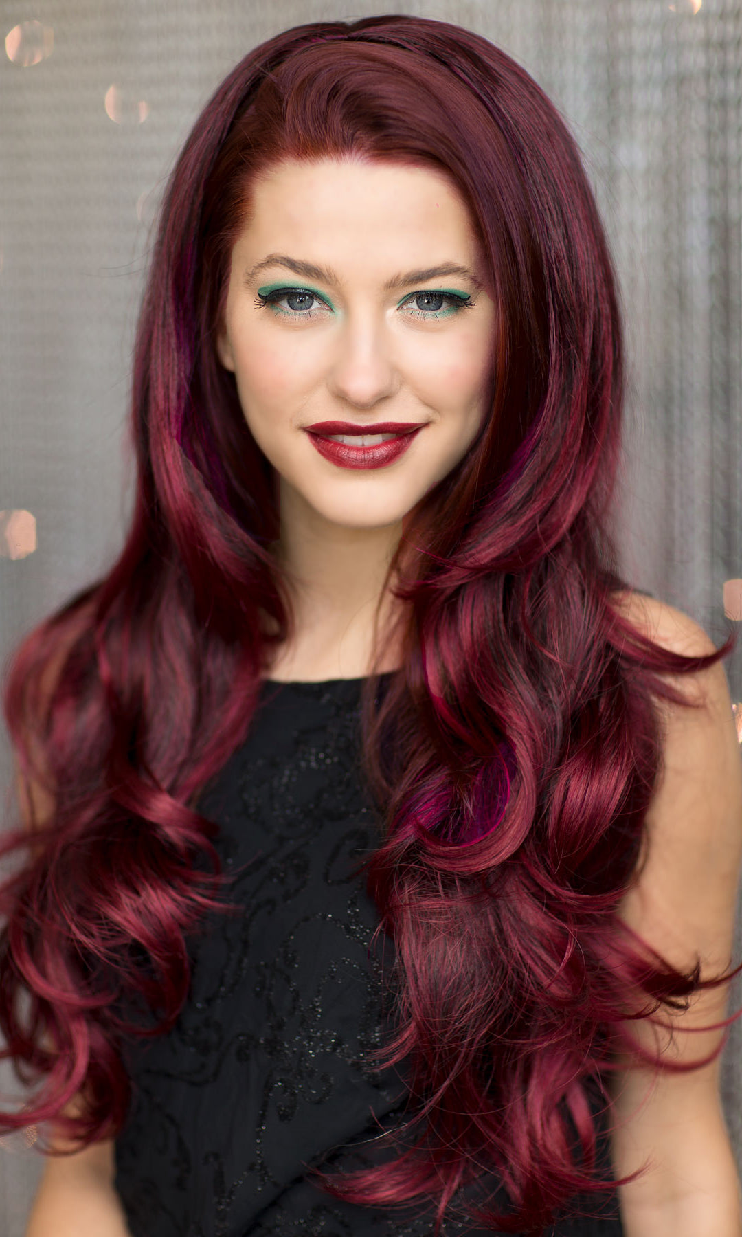 Woman with long, wavy, burgundy hair against a neutral background. Black and red half wig hairpiece (3/4 wig), loose curls: Monica