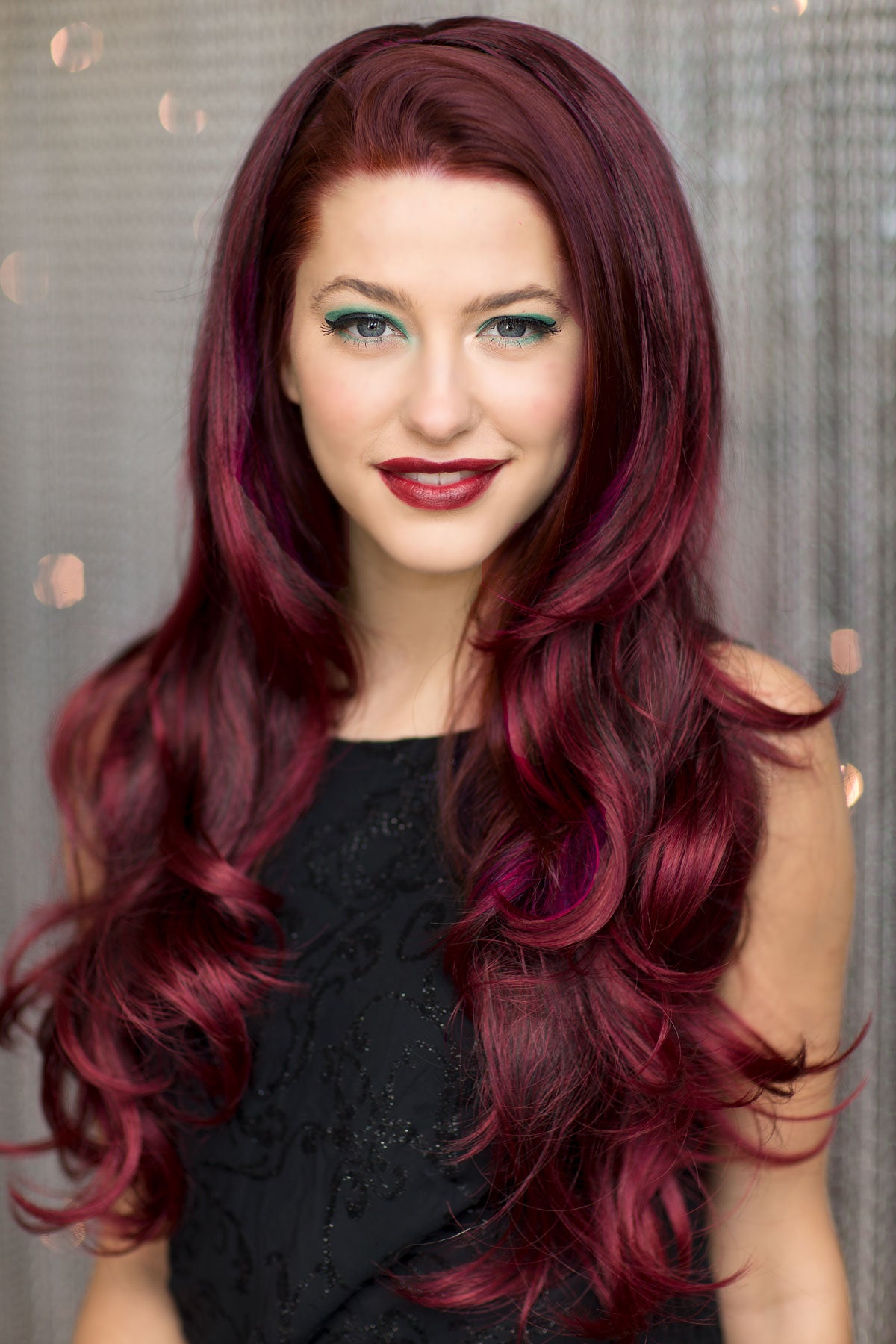 Woman with long, wavy, burgundy hair against a neutral background. Black and red half wig hairpiece (3/4 wig), loose curls: Monica
