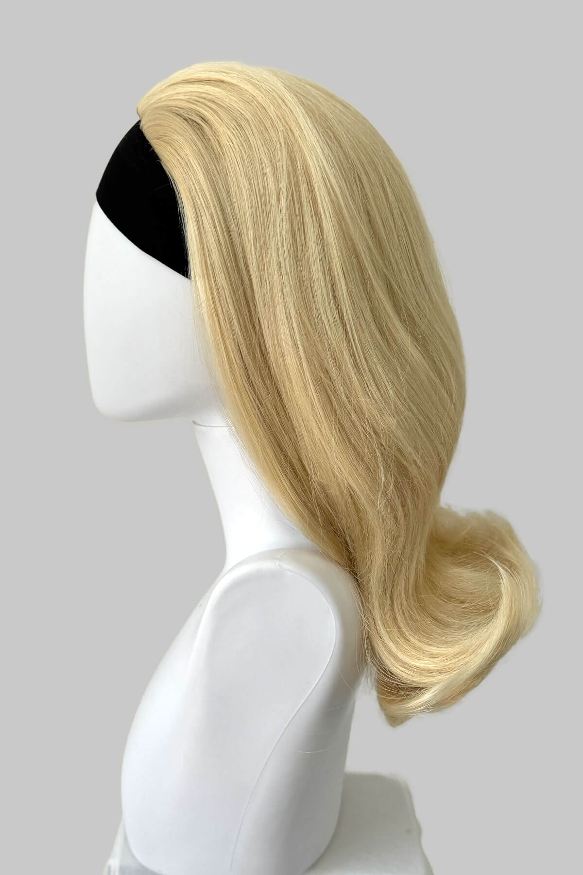 Blonde wig on a mannequin head against a gray background. 1960s half wig hairpiece, flicked, hair flip: Philippa blonde 613