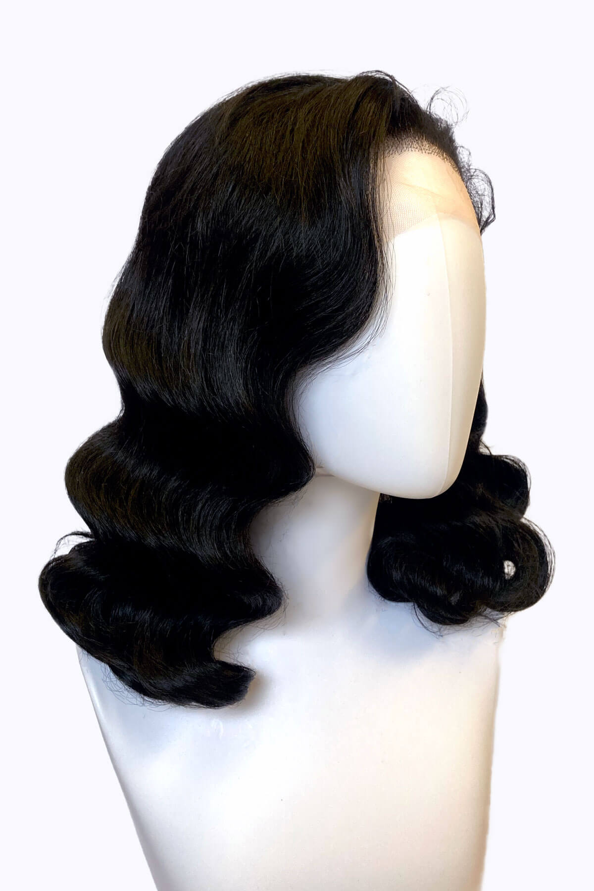 Black wig on a mannequin head against a white background. Black pinup wig, lace front with long finger waves: Tyra