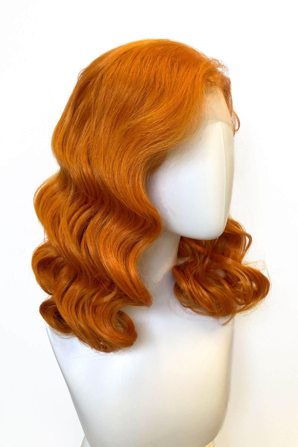 Orange wig on a mannequin head against a white background. Ginger pinup lace front wig, Dita Von Teese style vintage style wig with finger waves Lula