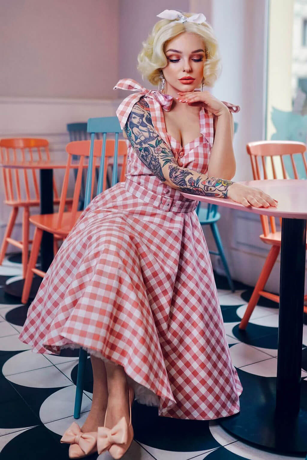 Woman in a red and white checkered dress sitting at a table in a cafe. Blonde pinup wig, lace front, vintage style: Marilyn creamy blonde 613