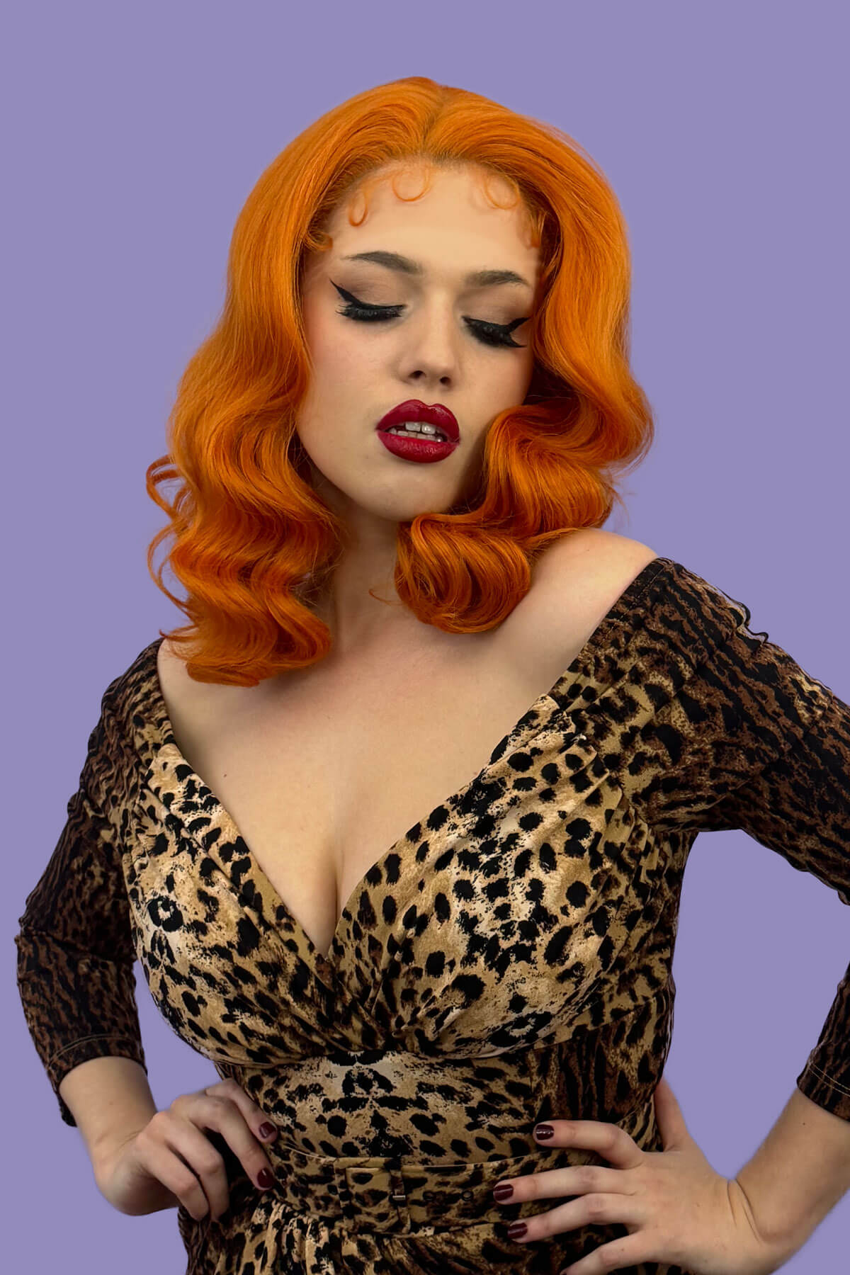 Woman with vibrant orange hair and red lipstick wearing a leopard print dress against a purple background. Ginger pinup lace front wig, Dita Von Teese style vintage style wig with finger waves Lula