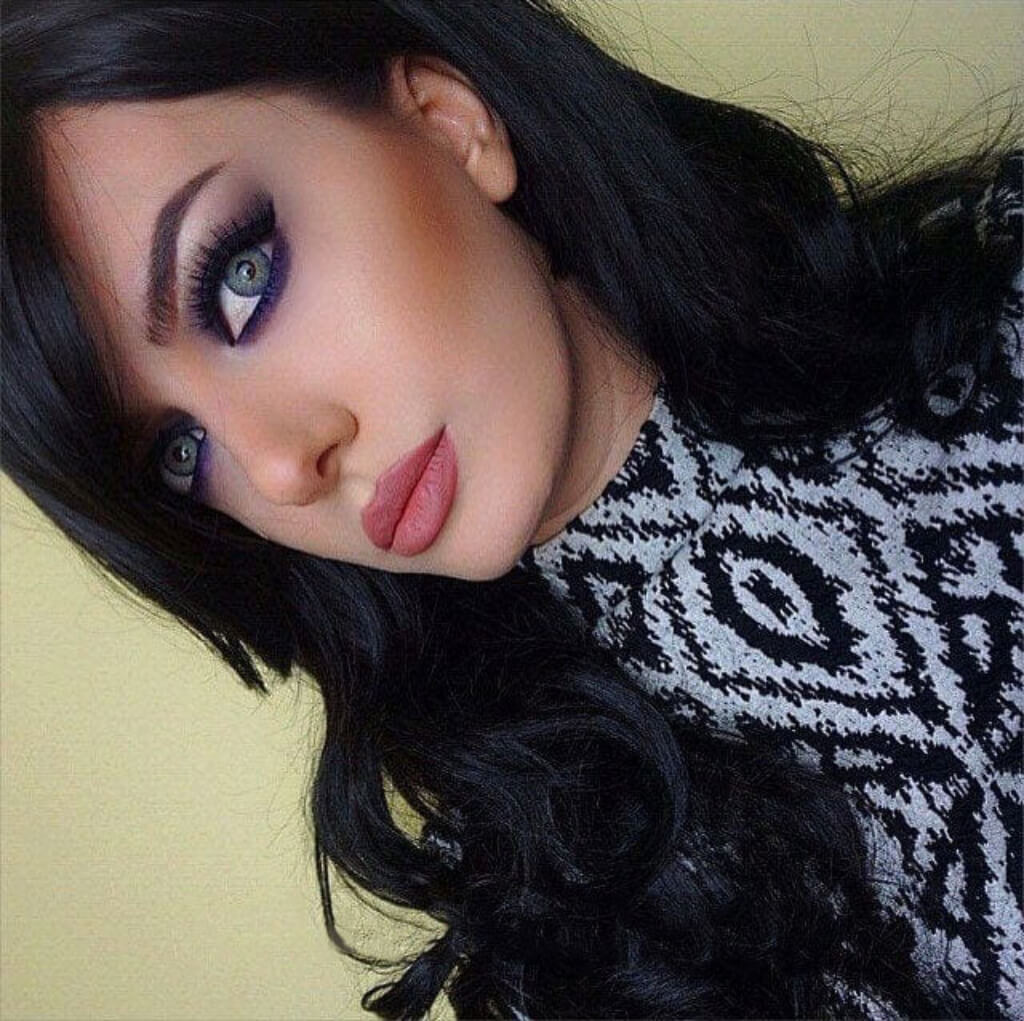 Close-up of a person with dark hair and patterned sweater on a light background. Long wavy black wig with side-sweeping Fringe: Charlotte
