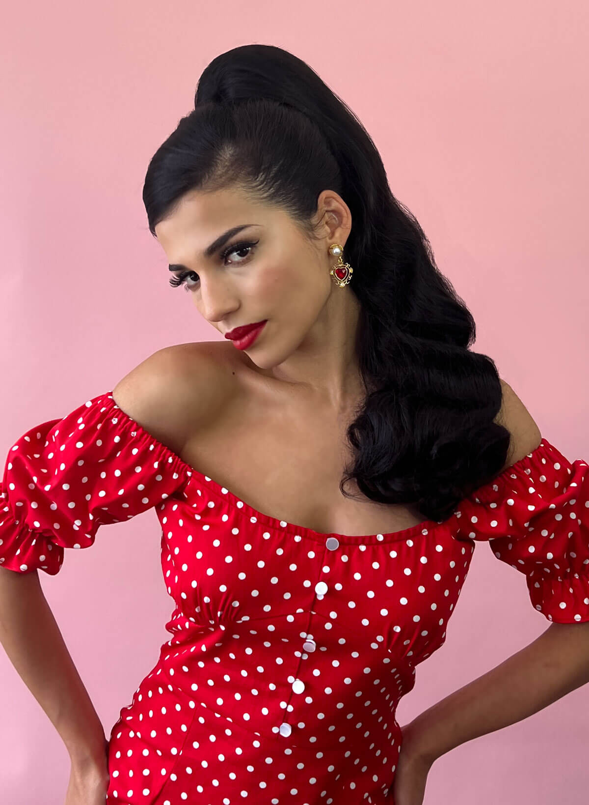 Woman wearing a red polka dot dress against a pink background. Black Retro style ponytail hairpiece, long with vintage waves: Arabella black 1B
