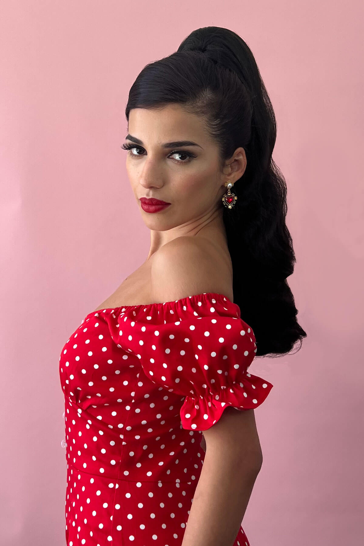 Woman wearing a red polka dot dress against a pink background. Retro style ponytail hairpiece, long with vintage waves: Arabella dark brown 4